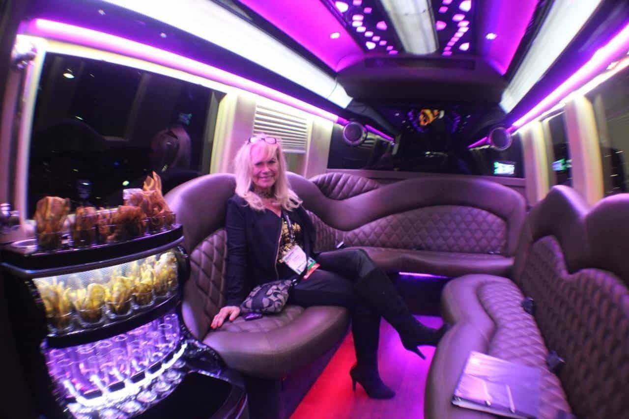Woman sitting in a purple-lit limousine with plush leather seats and neon ceiling lights