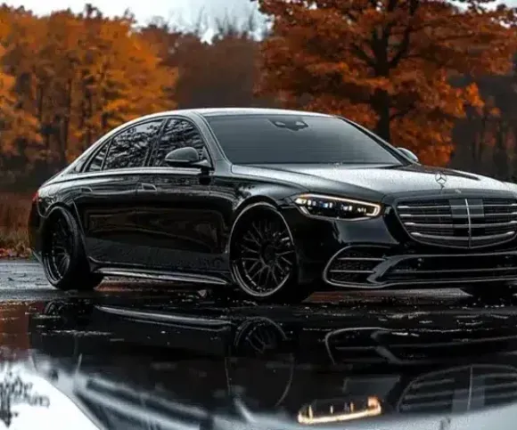 Black luxury sedan parked on wet pavement with autumn trees reflected in the foreground