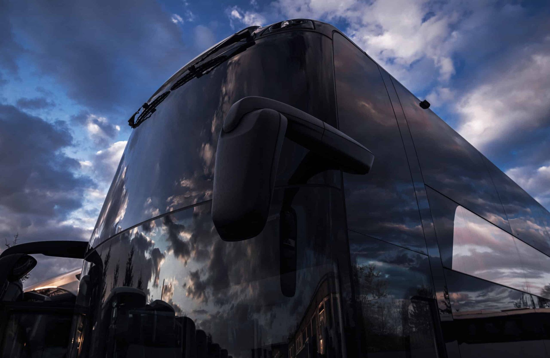 Dark coach bus with reflective windows parked under a cloudy dusk sky