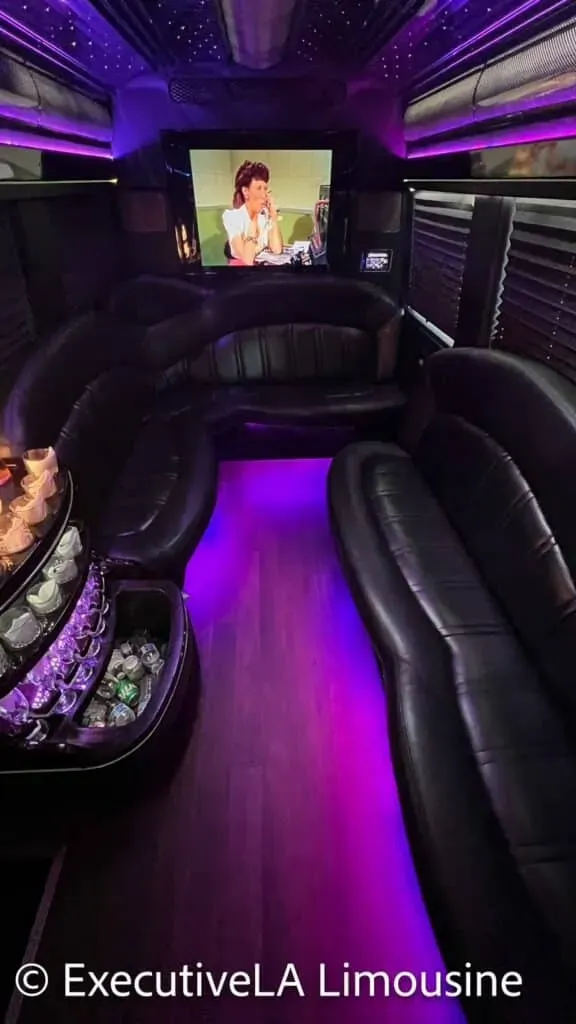 Purple-lit limousine interior with black leather seats and a TV screen at the front.