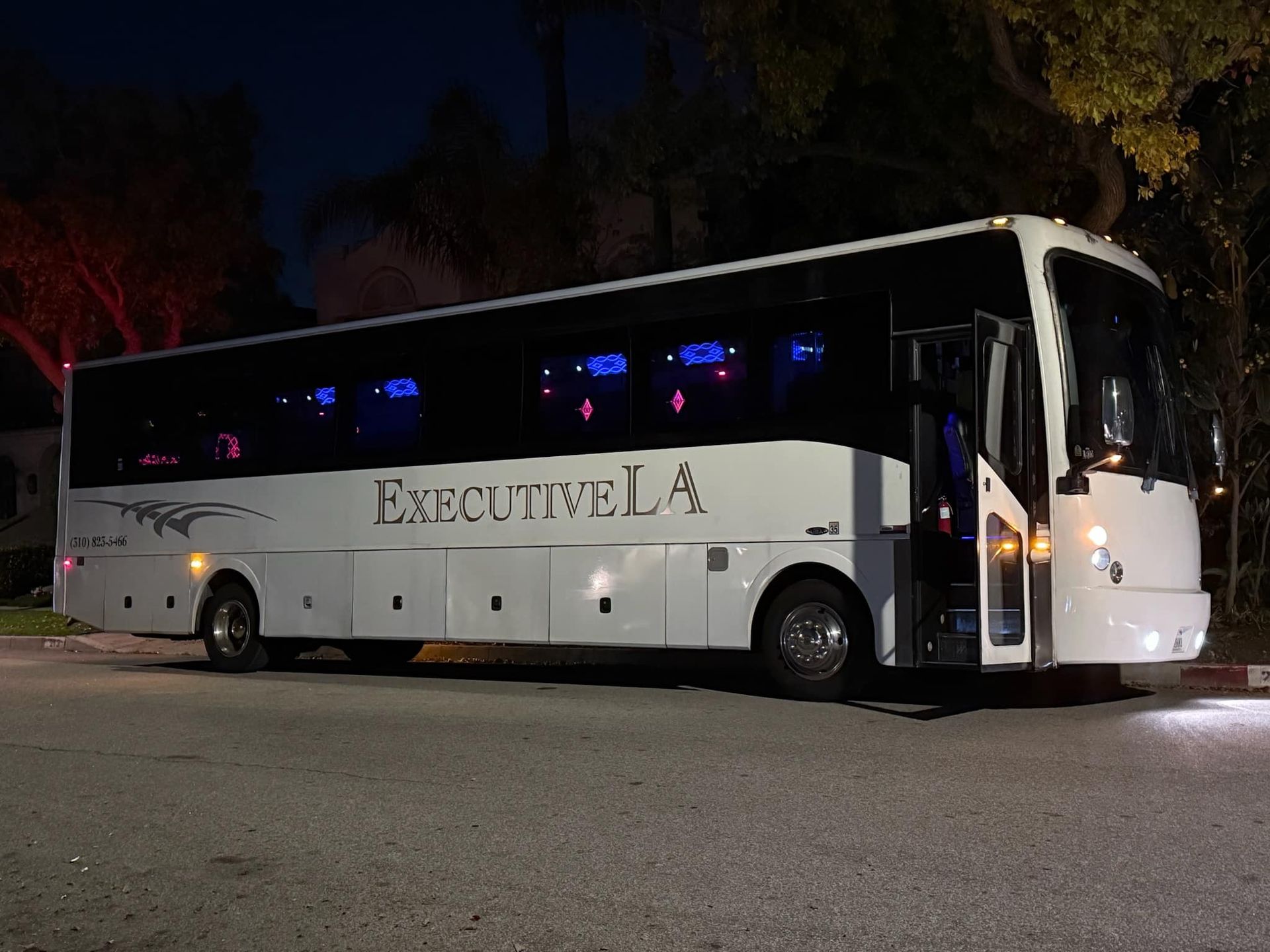 White Executive Line coach bus parked at night under trees, illuminated by interior lights