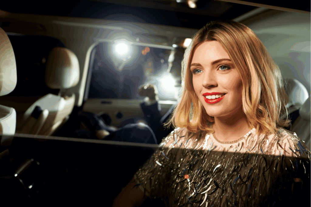 Woman smiling in a car at night, wearing a glittery top with warm interior lights.