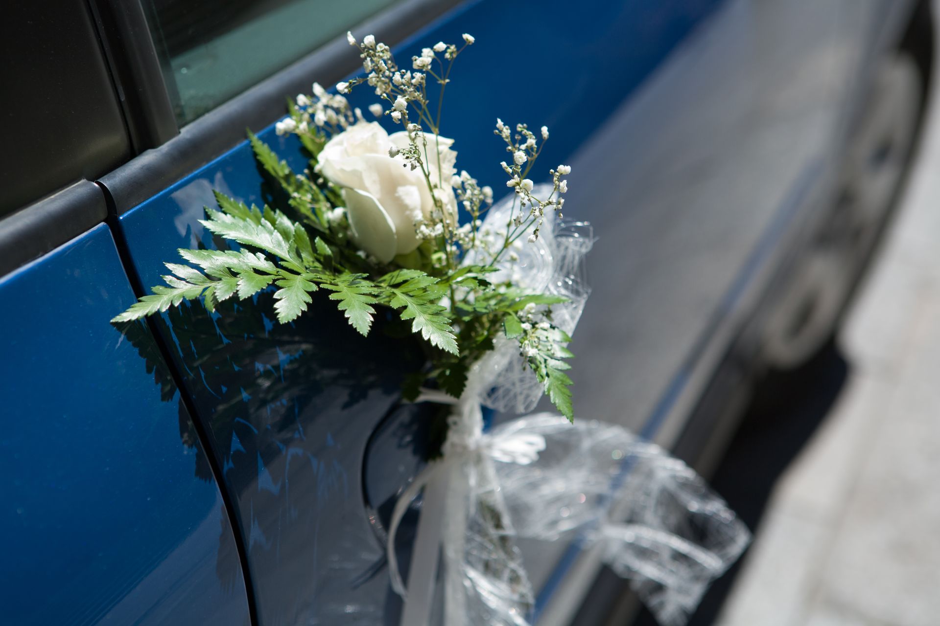 White floral arrangement with ribbon tied to a blue car door handle