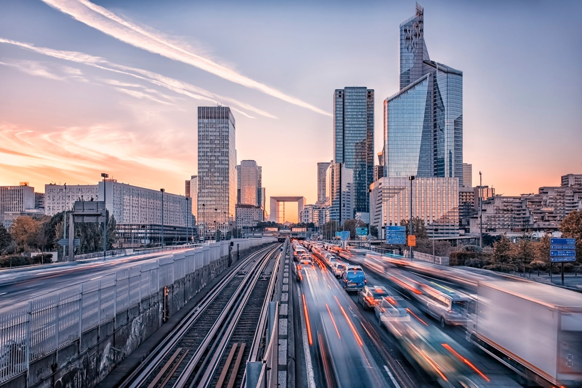 City skyline at dusk with tall modern buildings and blurred traffic on a busy highway below