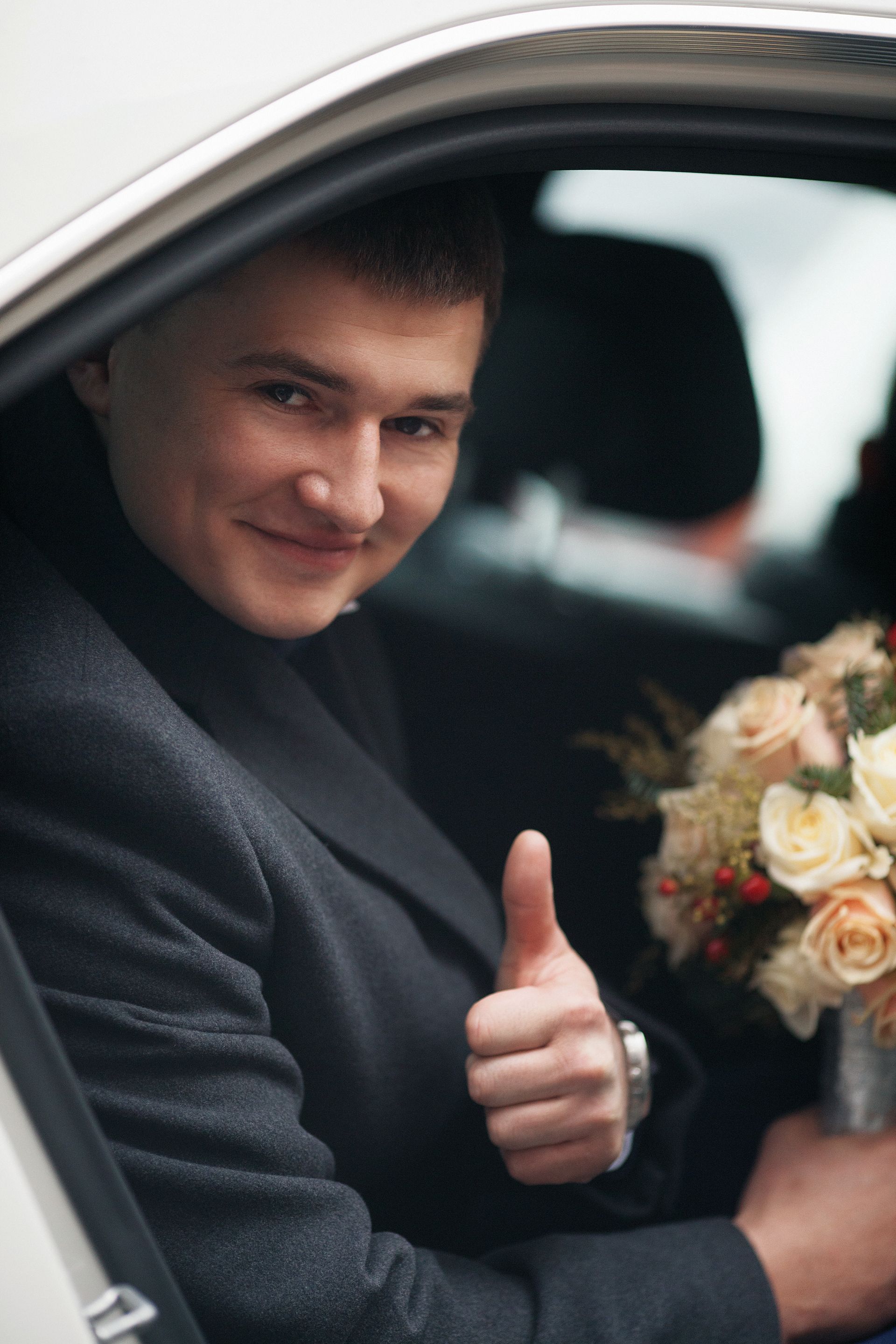 Man in a car giving a thumbs-up and holding a bouquet of flowers