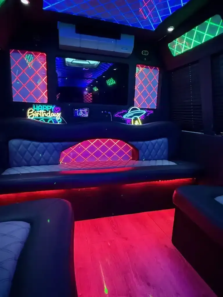 Neon-lit party bus interior with quilted bench seating, red floor lighting, and colorful LED ceiling panels.