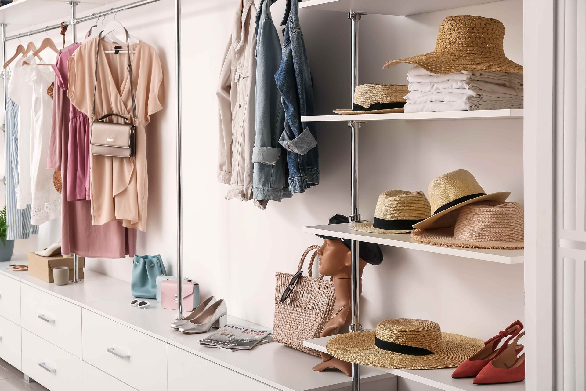 Bright walk-in closet with hanging clothes, white shelves, straw hats, shoes, and woven bags