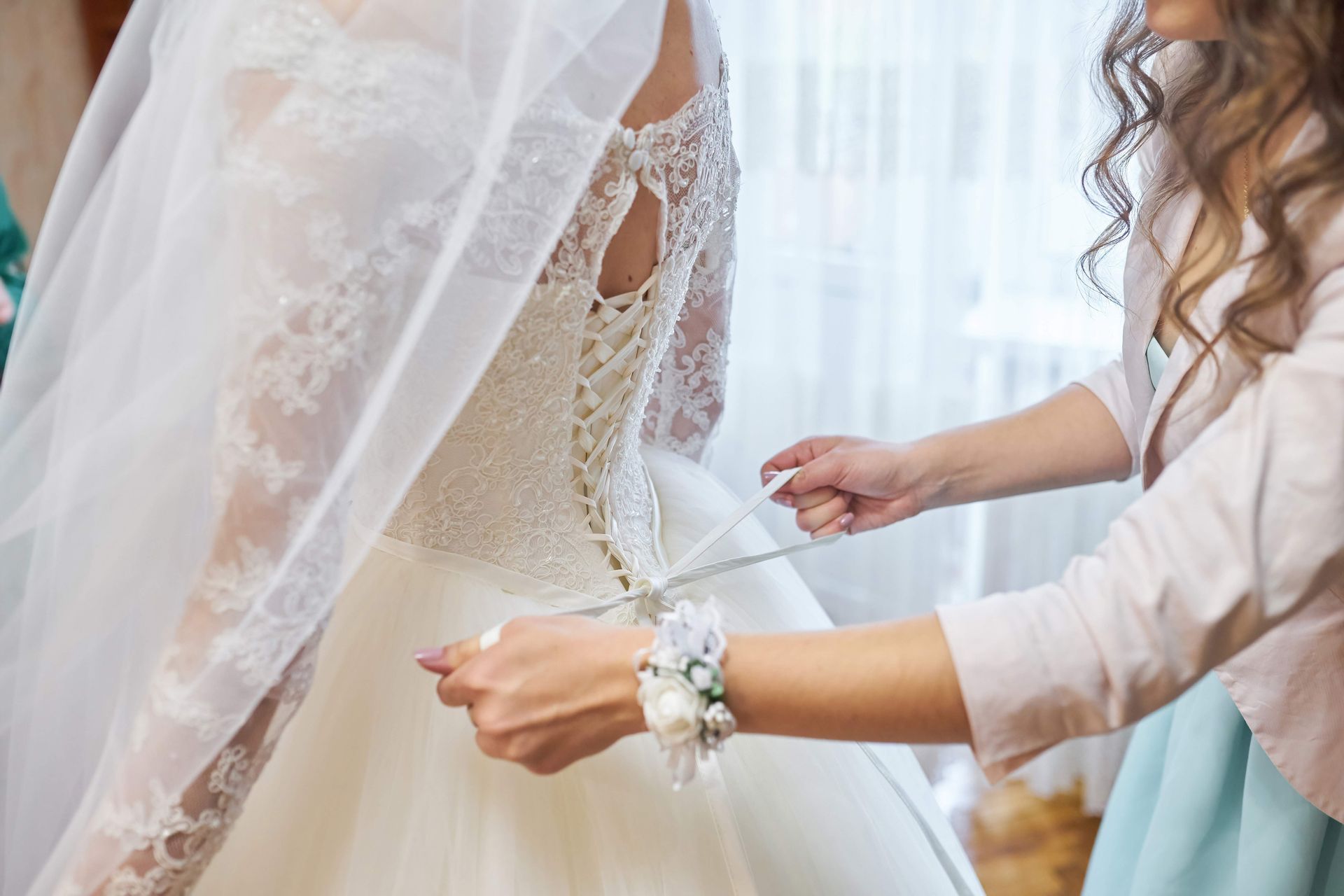 Woman fastening the back of a wedding dress while another adjusts the veil