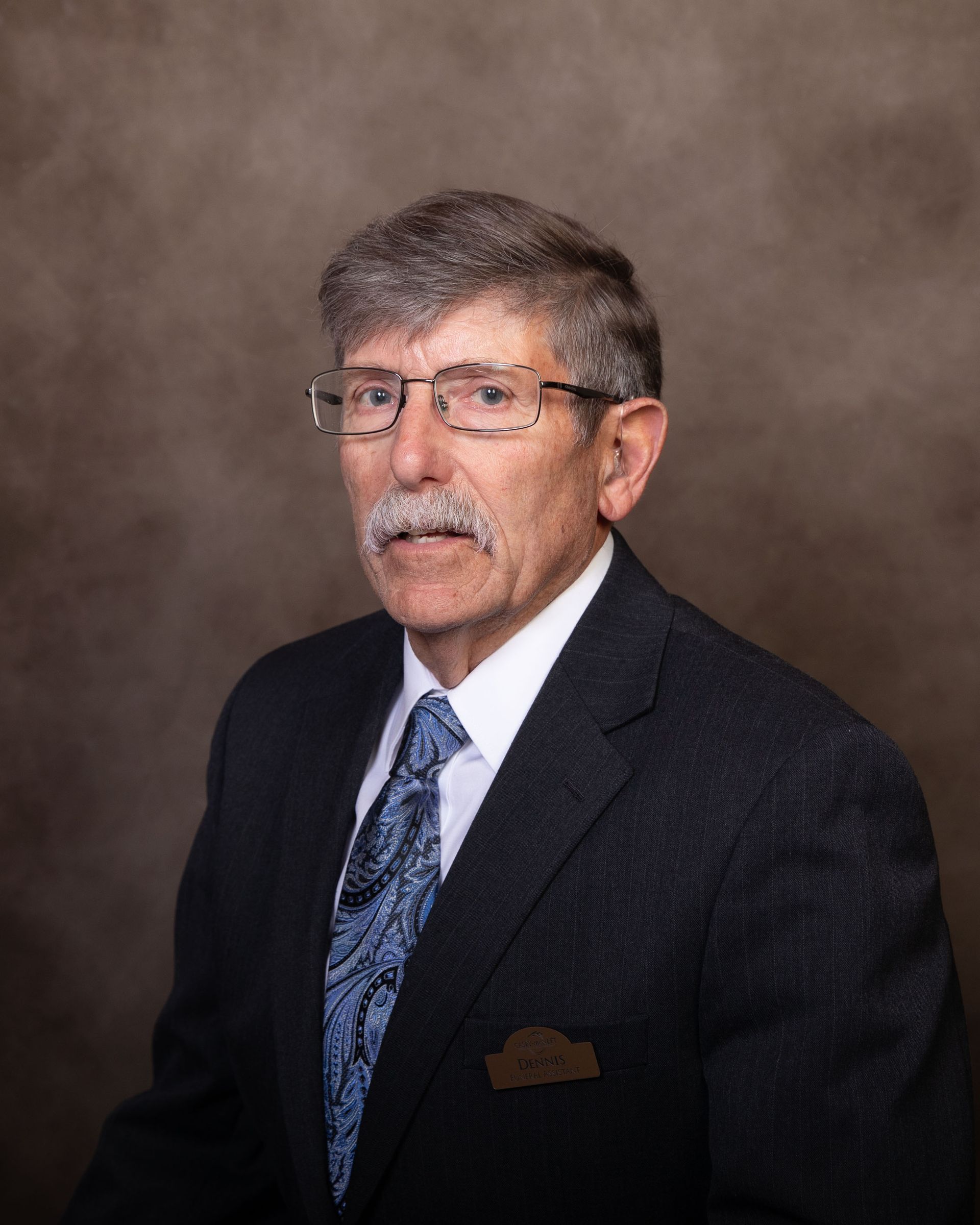 A man with glasses and a mustache is wearing a suit and tie.