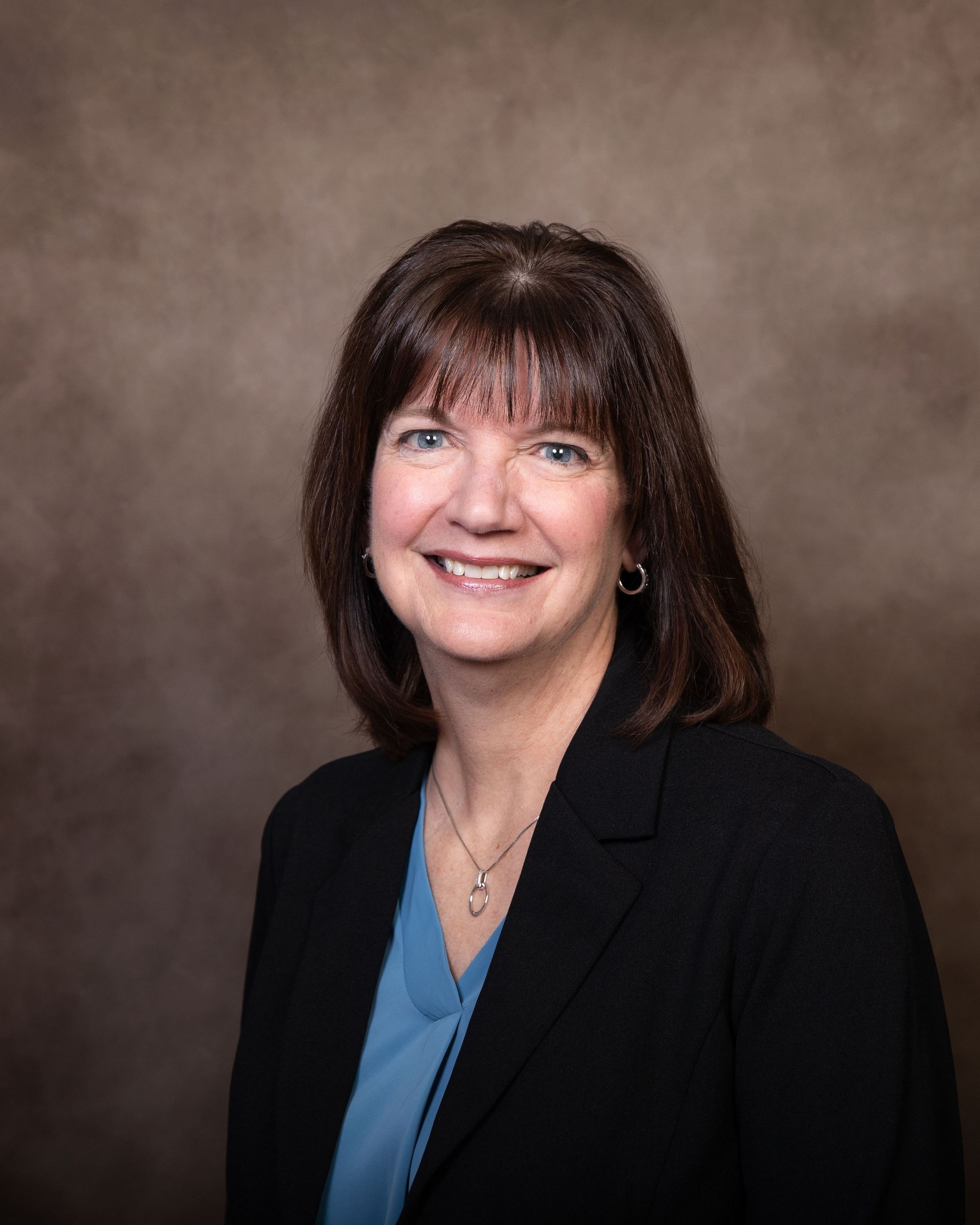 A woman in a blue shirt and black jacket is smiling for the camera.