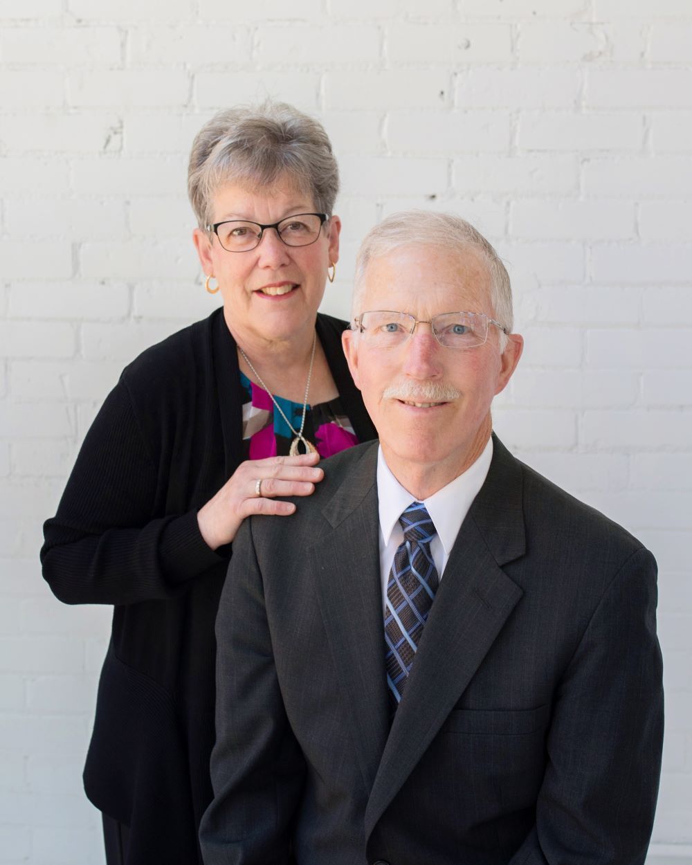 A man in a suit and tie is standing next to a woman in a black sweater.