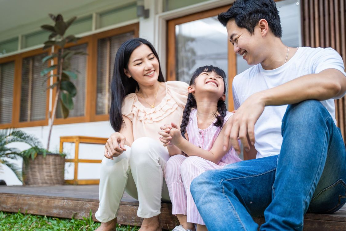 Three people sitting on steps outside a house, smiling and talking together.