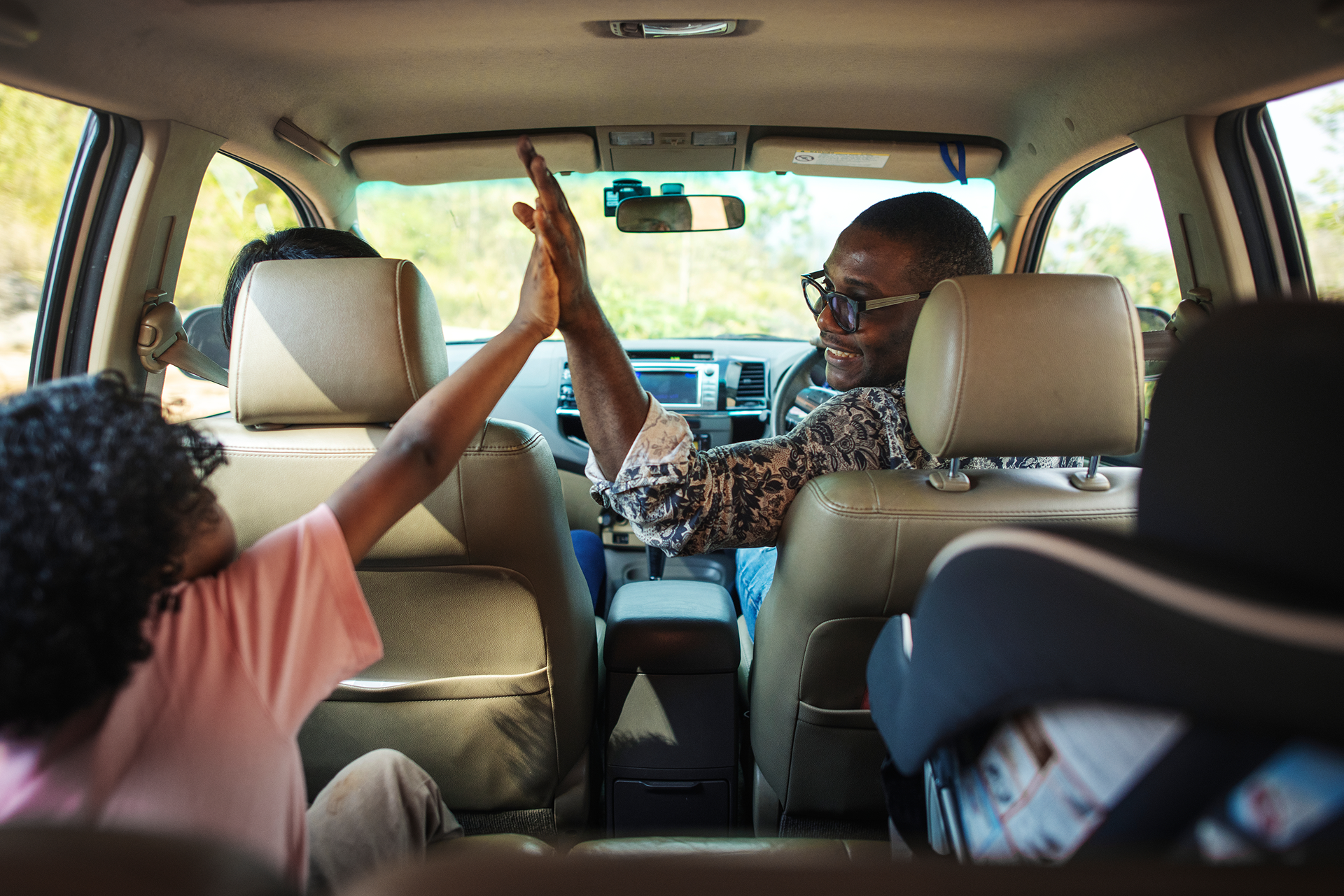 People high-five in a van’s back seat, with luggage and a driver visible in front.
