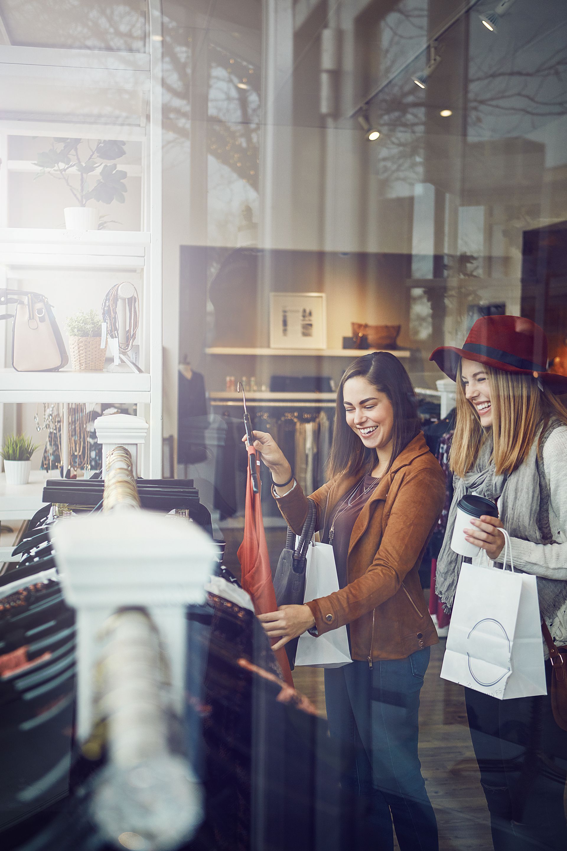 Two women shopping in a clothing store, smiling beside a rack of coats.