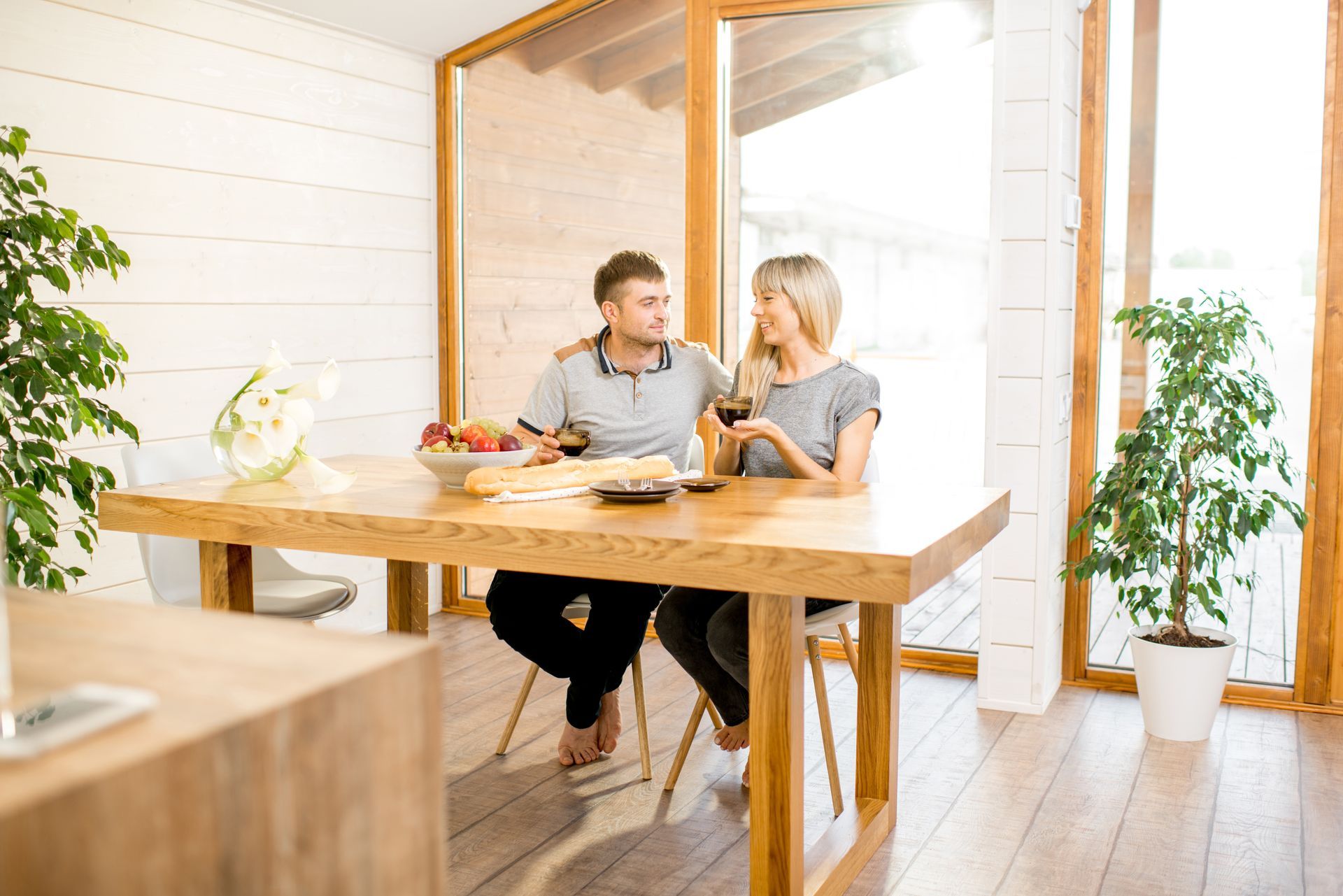 Two people talking at a wooden table in a bright, white office with plants.