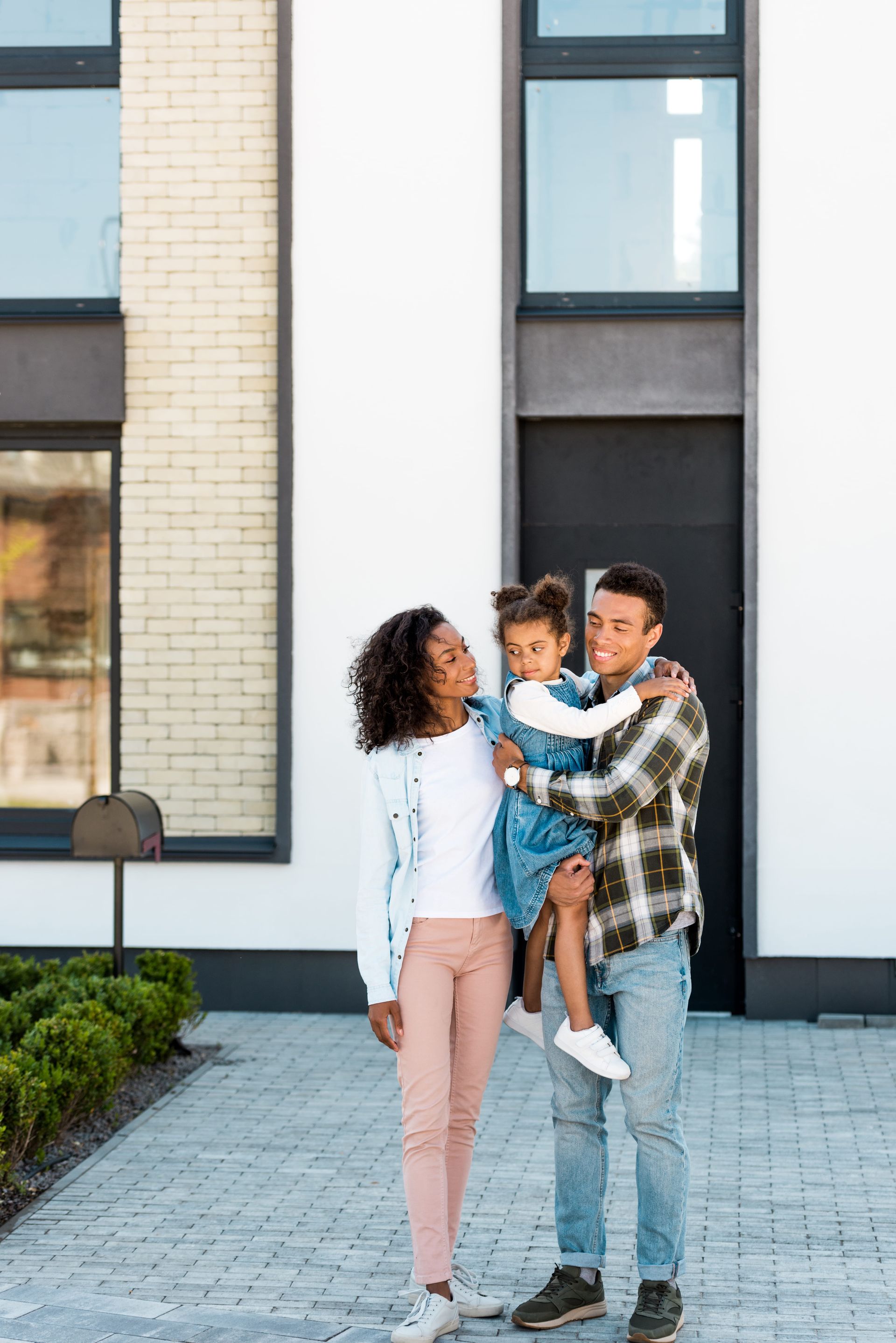 Family standing outside a modern building, parents holding a young child in the center
