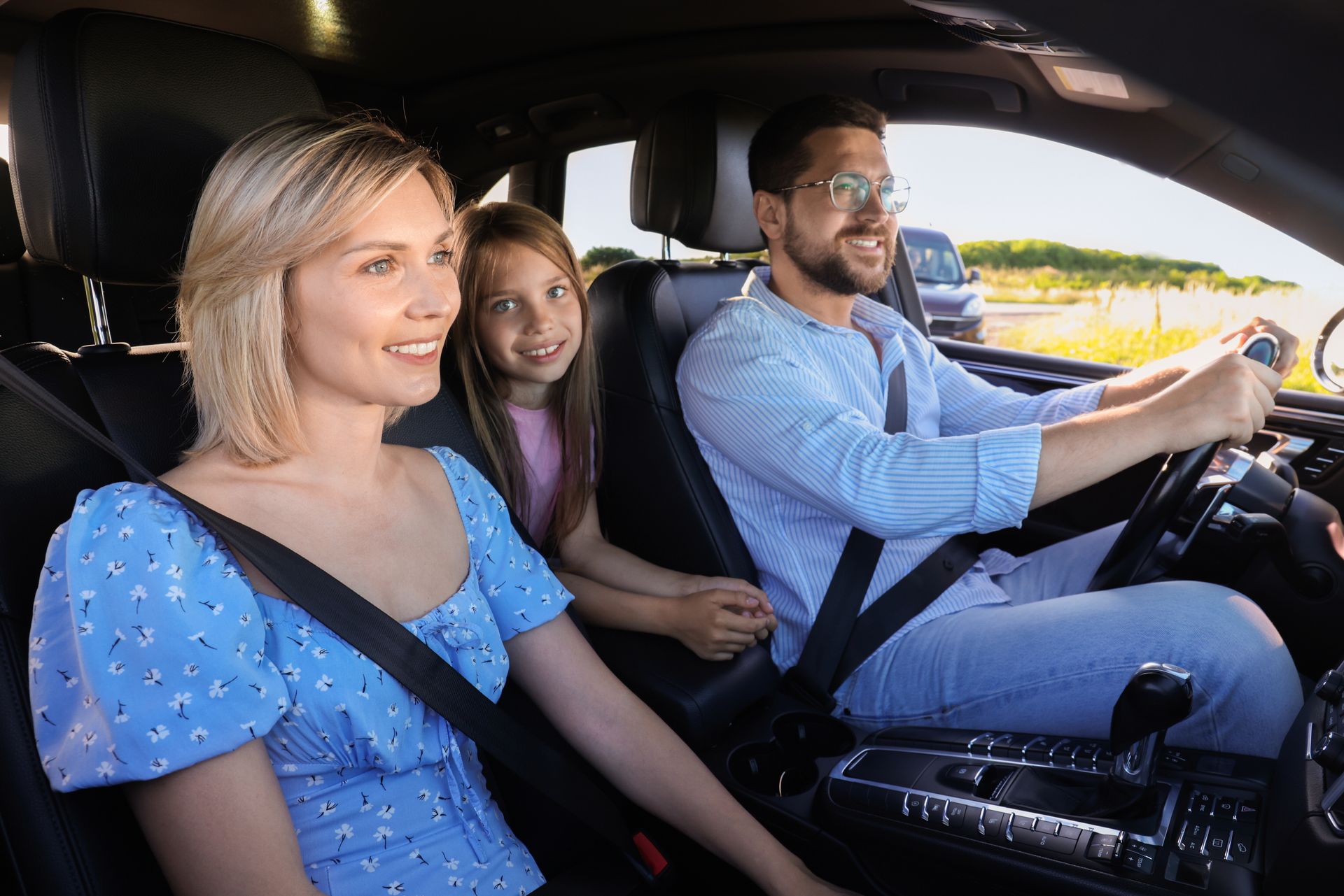 Three people wearing seatbelts riding in a car, with the driver and front passenger smiling.
