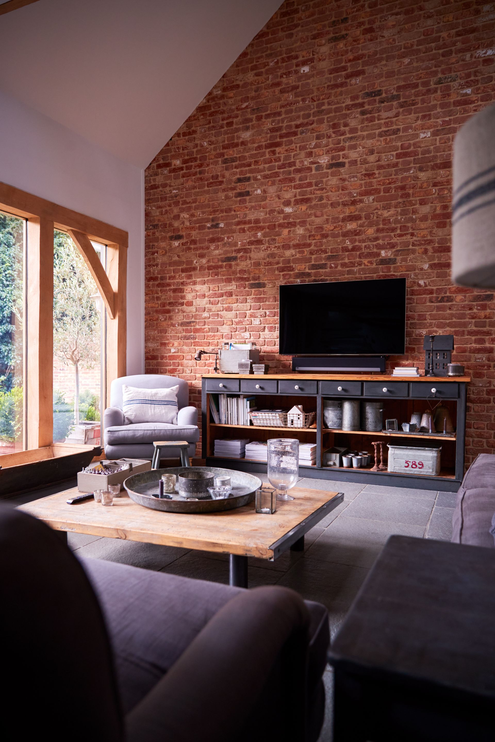 Living room with exposed brick wall, TV, fireplace, and large windows letting in natural light