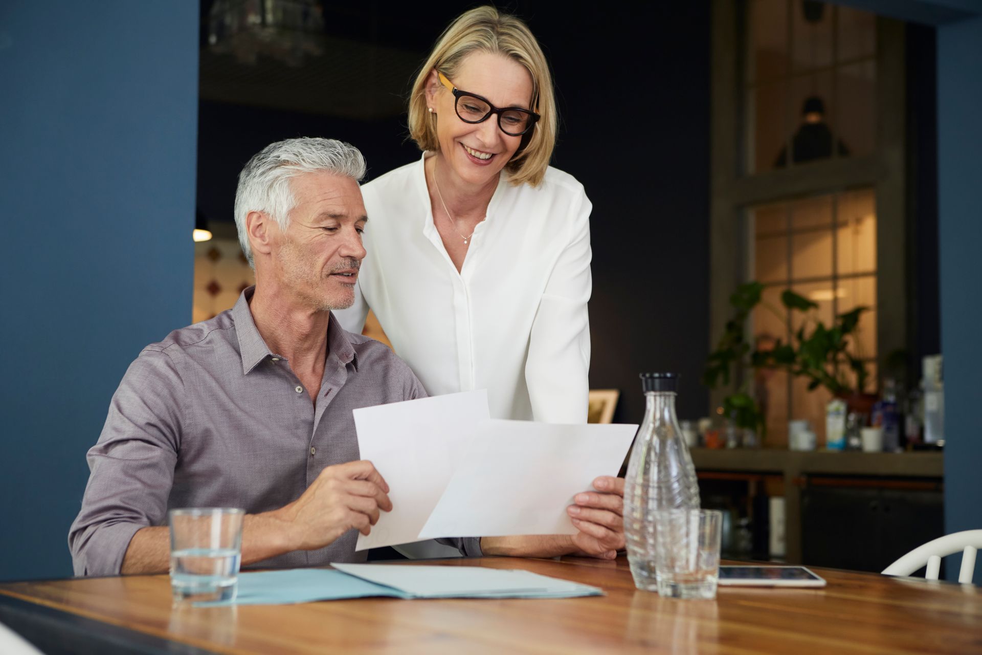 Two people reviewing documents at a table in a modern office, with a water bottle and glass nearby.