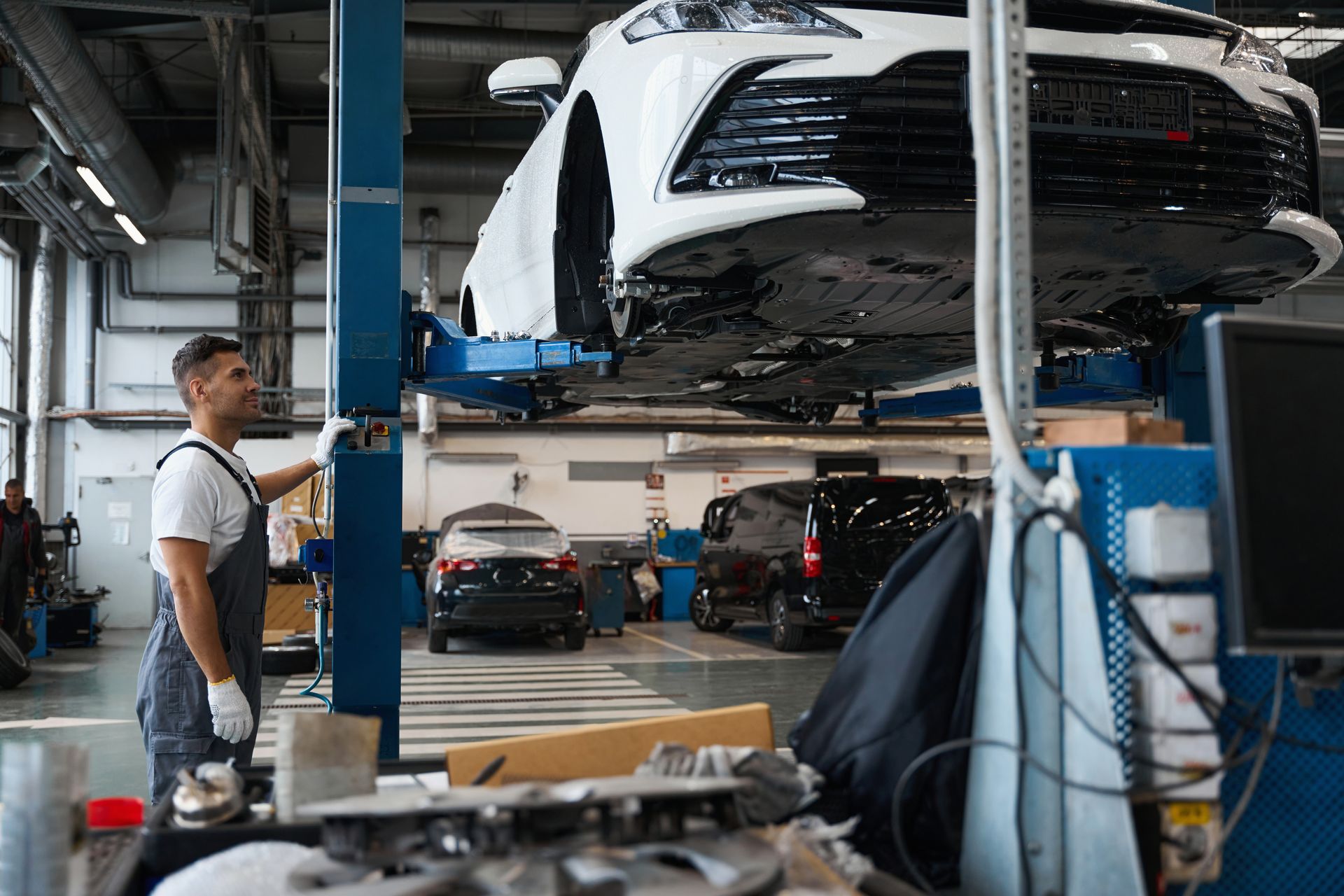 Mechanic in an auto repair shop inspecting a car lifted on a blue hydraulic lift