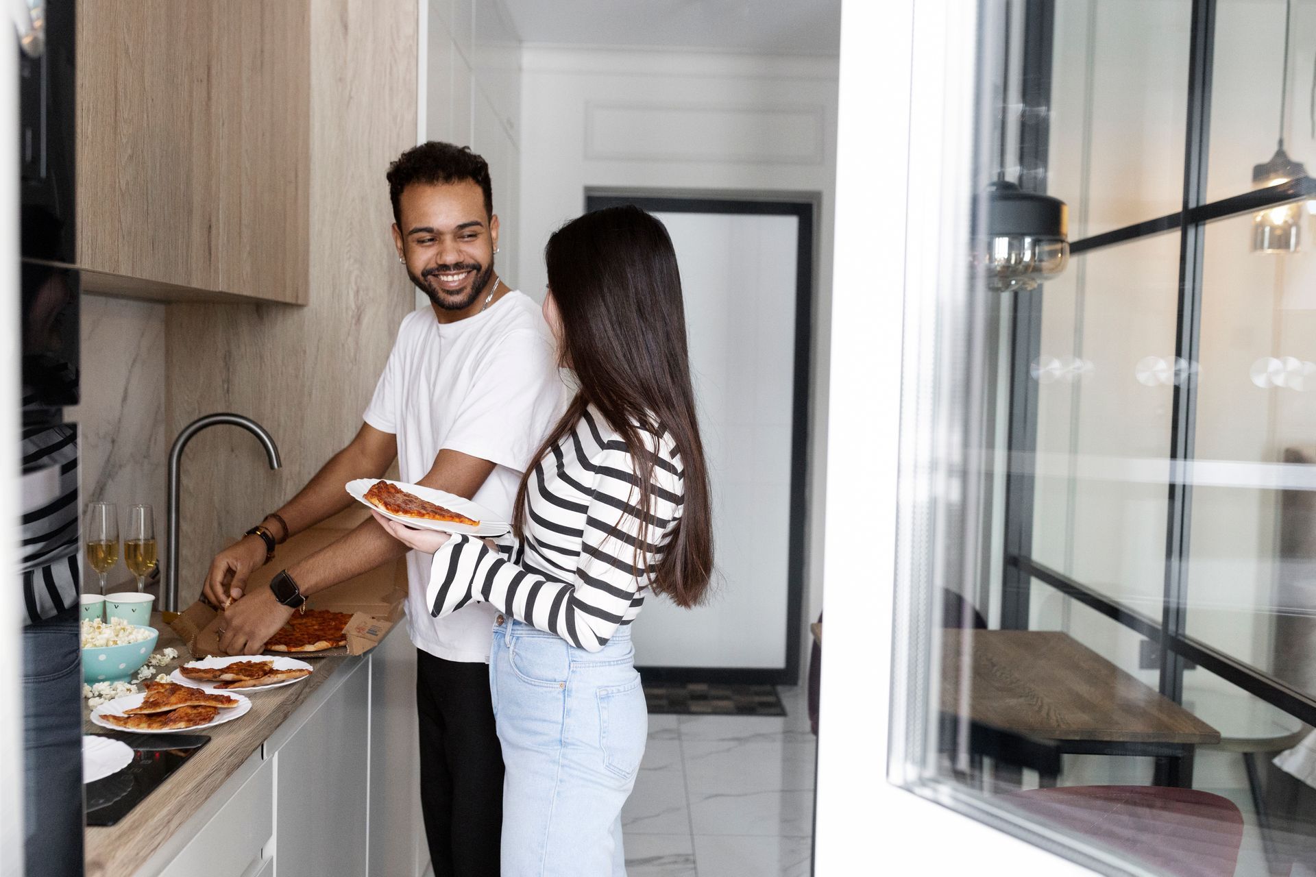 Two people cooking together in a bright modern kitchen, smiling by the sink and counter.