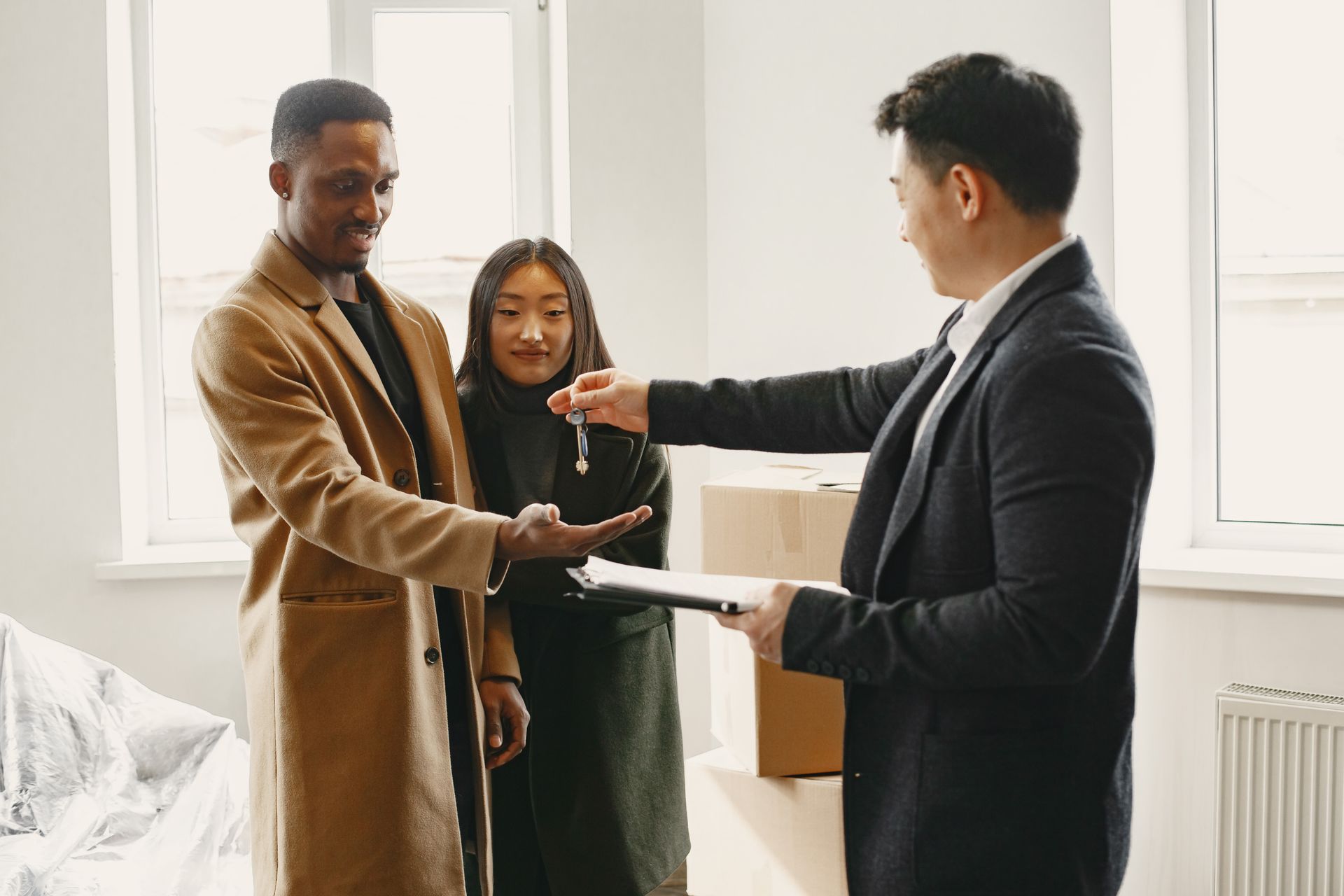 Two people shake hands with a realtor in a bright apartment, documents in hand.