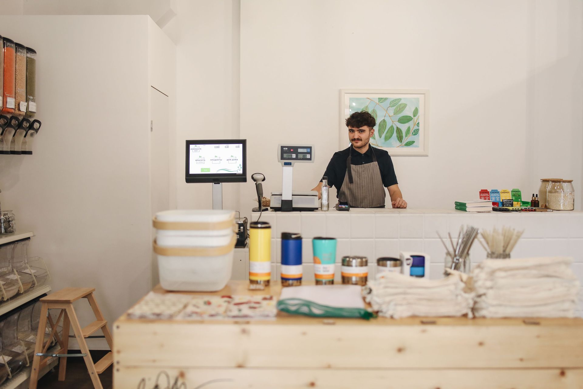 Person working behind a counter in a bright craft studio with jars, tools, and shelves of supplies