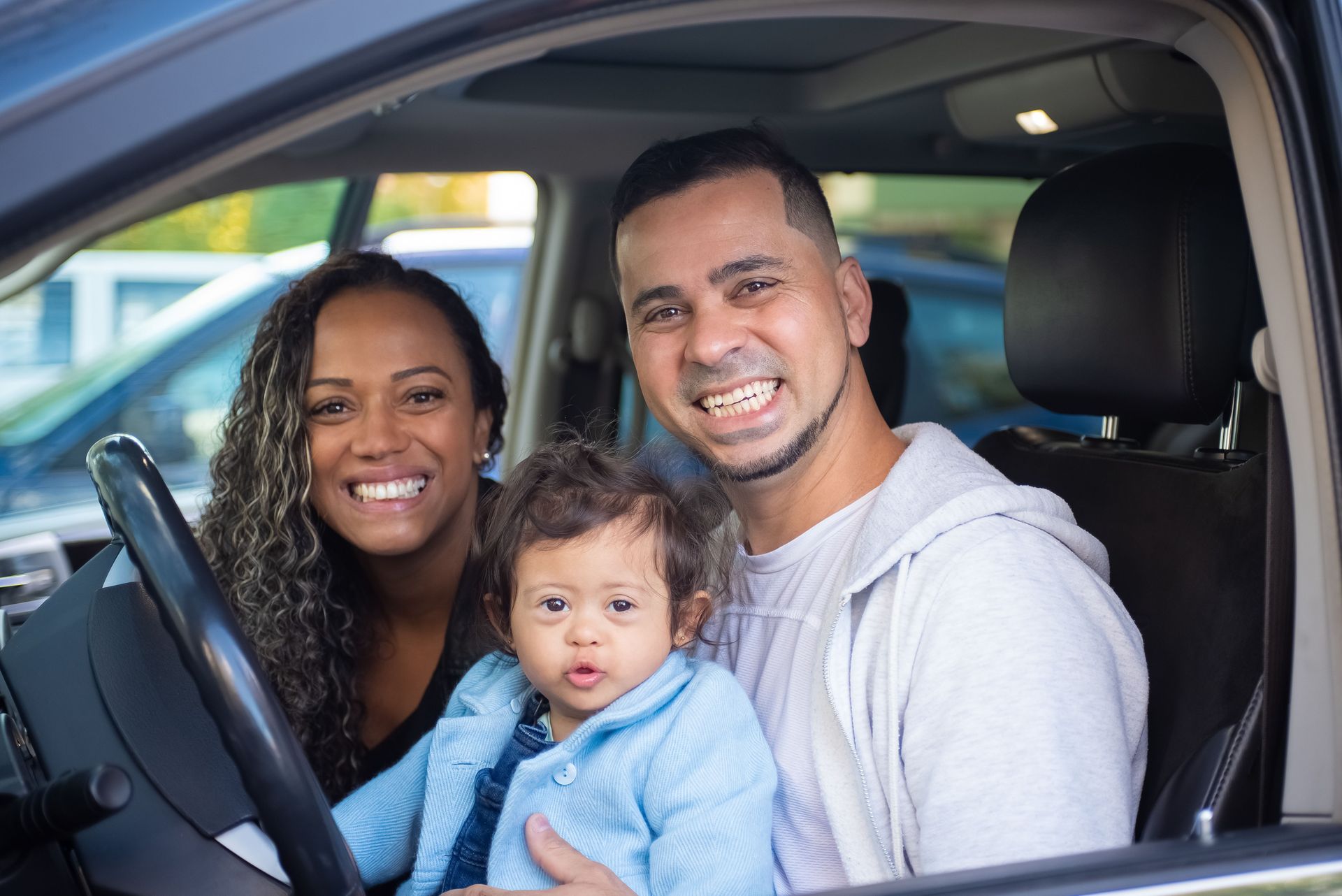 Family smiling beside white car in a showroom, with arms raised in excitement