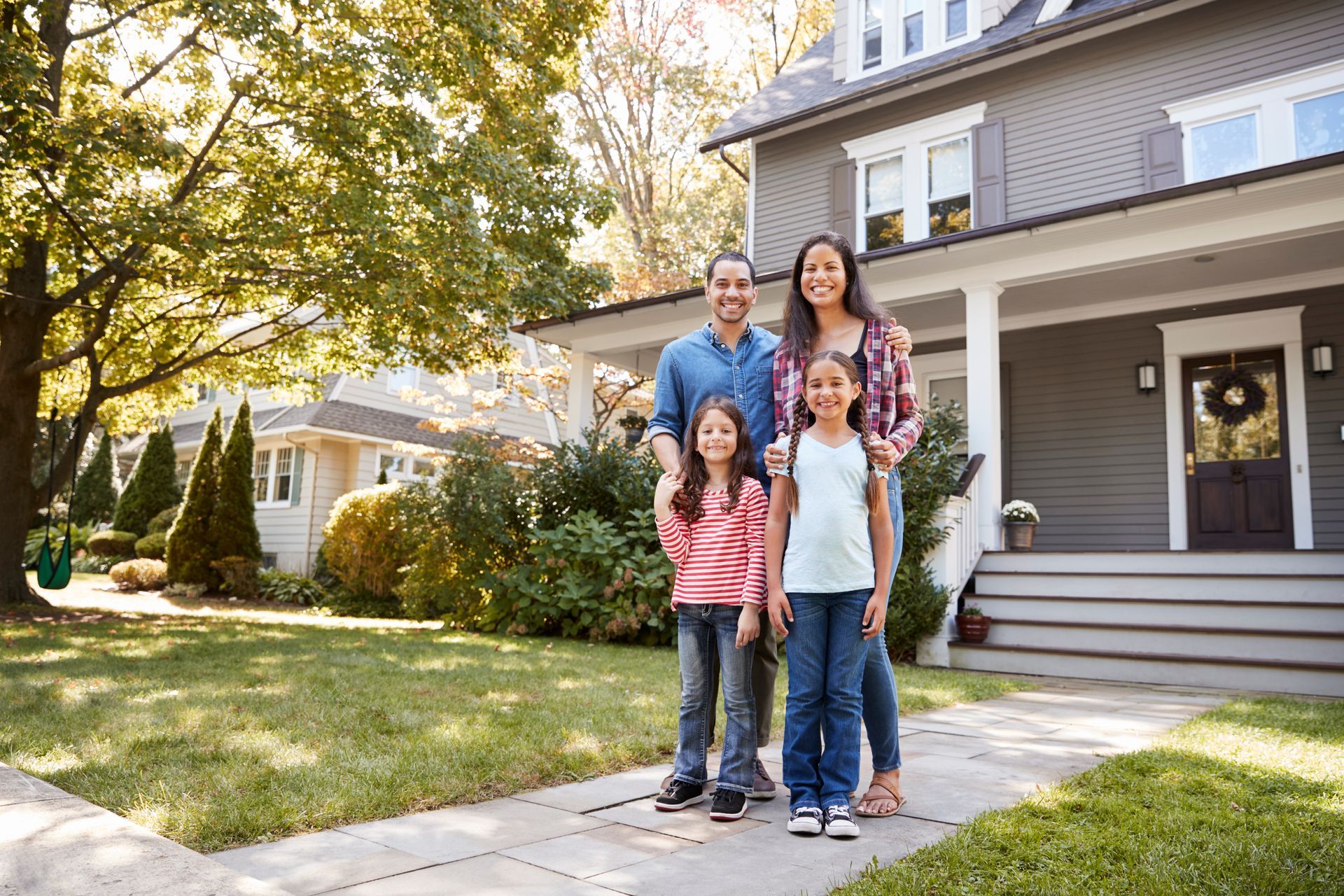 Family standing on a suburban front walk in front of a house, smiling in the sunlight