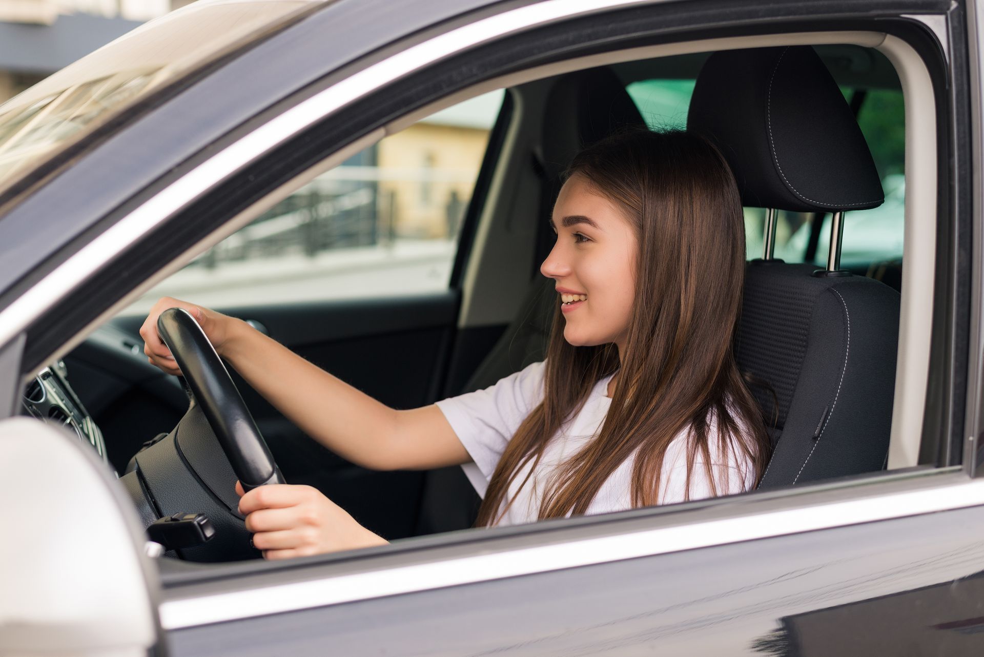 Young woman smiling while driving a car, viewed from the open driver-side window