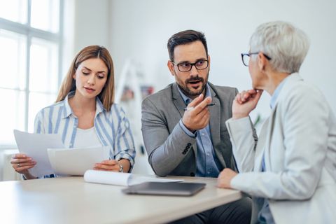 Three coworkers discussing documents at a desk in a bright office meeting room
