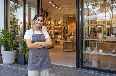 Smiling shop owner standing at the entrance of a cozy boutique with warm lights and plants