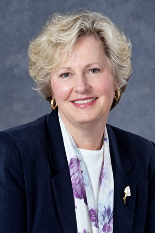Smiling professional in navy blazer and floral scarf against a gray studio backdrop