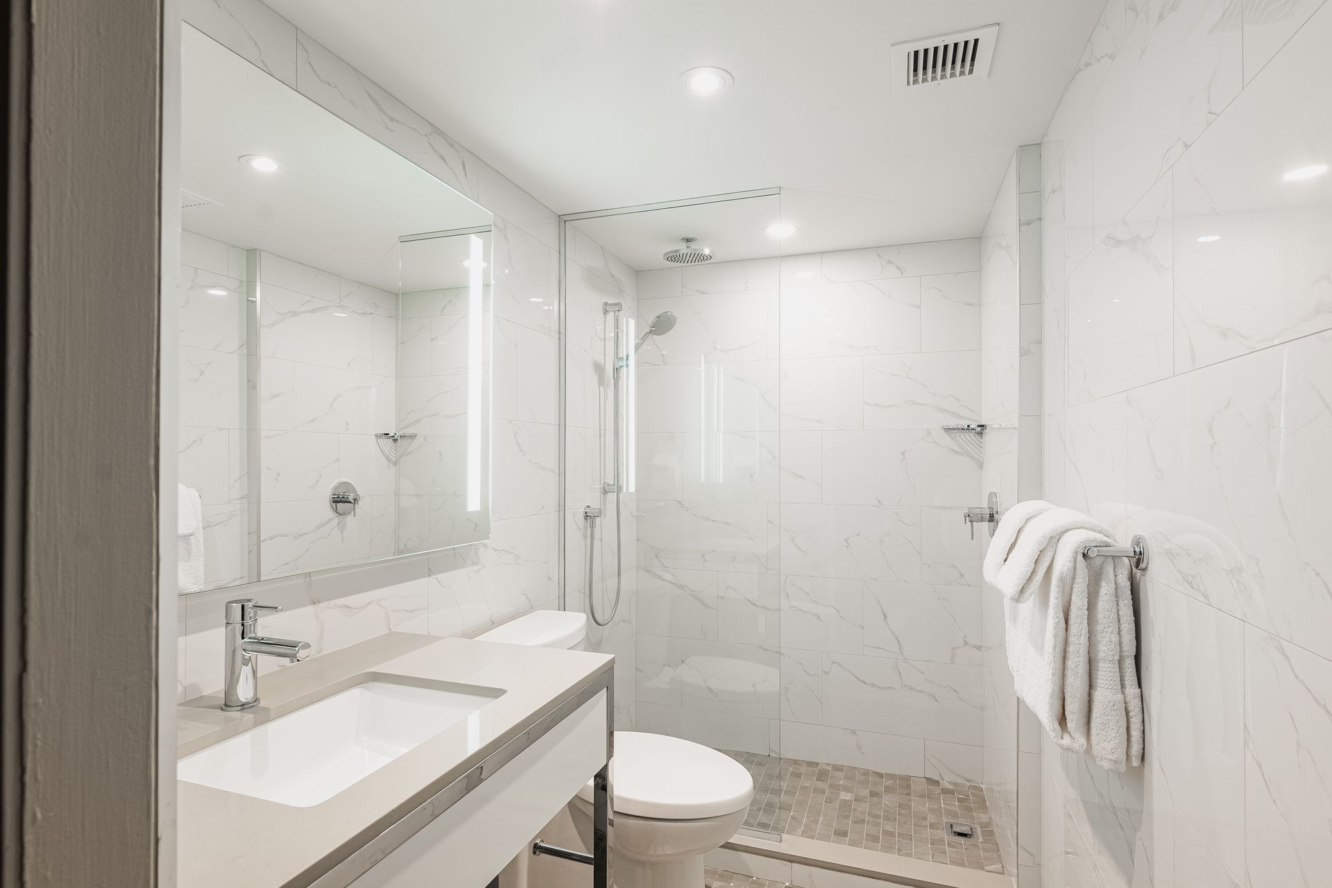 Une salle de bain avec WC, lavabo, miroir et douche à l'italienne.