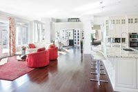 Un salon et une cuisine dans une grande maison avec parquet et armoires blanches.