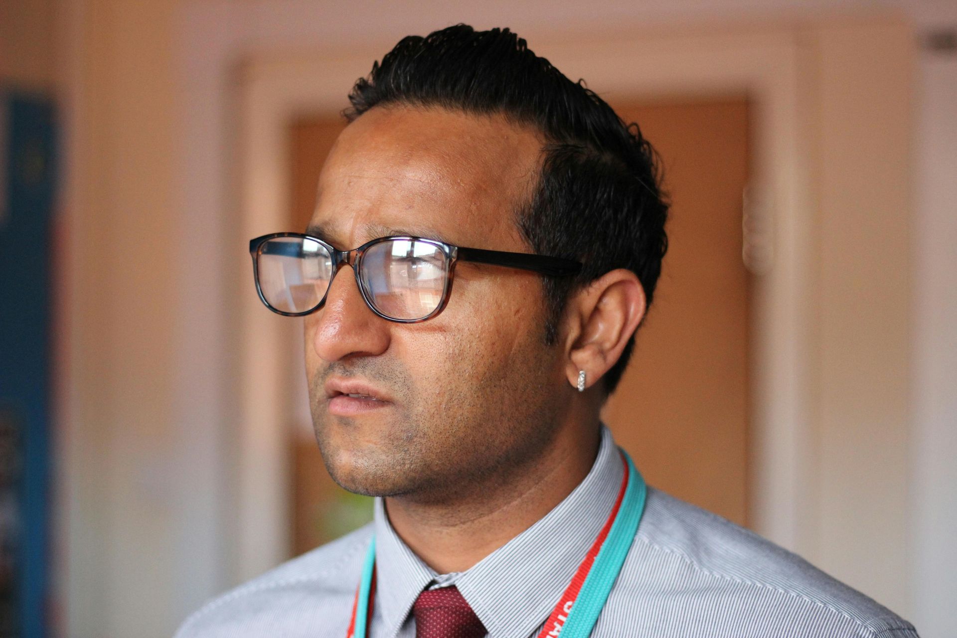Man wearing glasses and a lanyard, looking off-camera. He's in a light-colored shirt in a room.