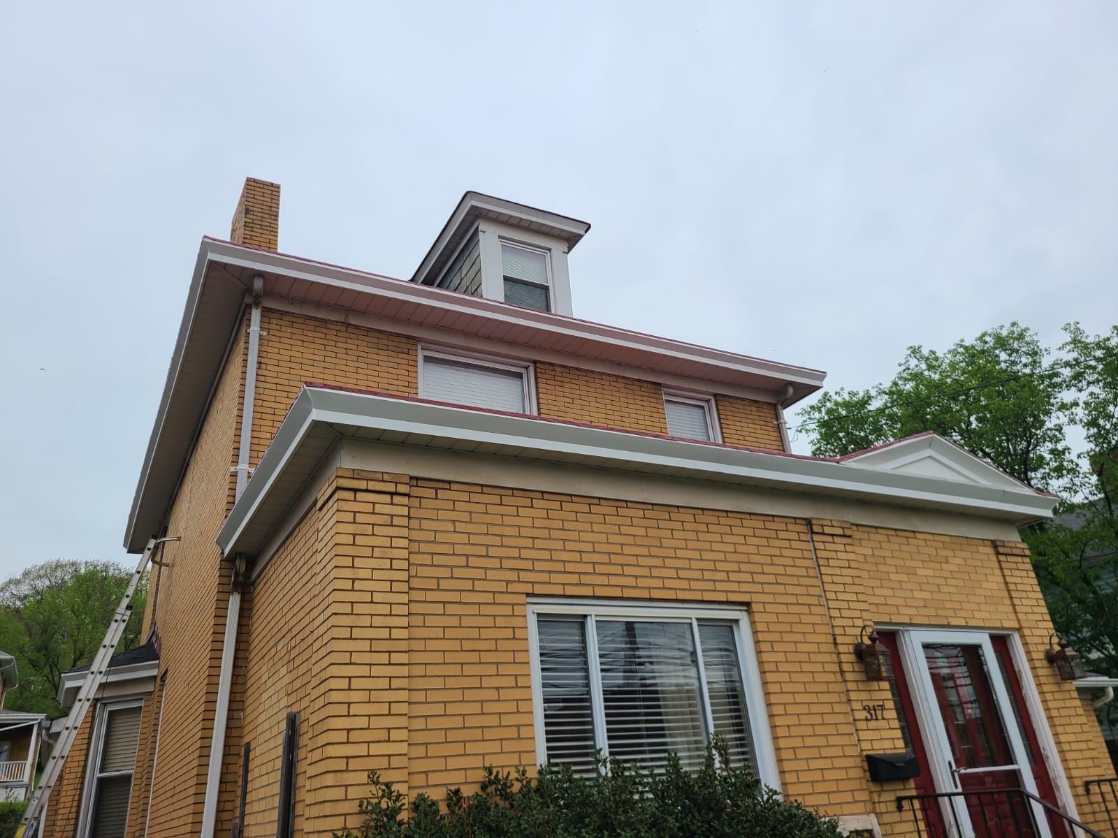 Two-story brick house with a dormer and gray trim against a cloudy sky.