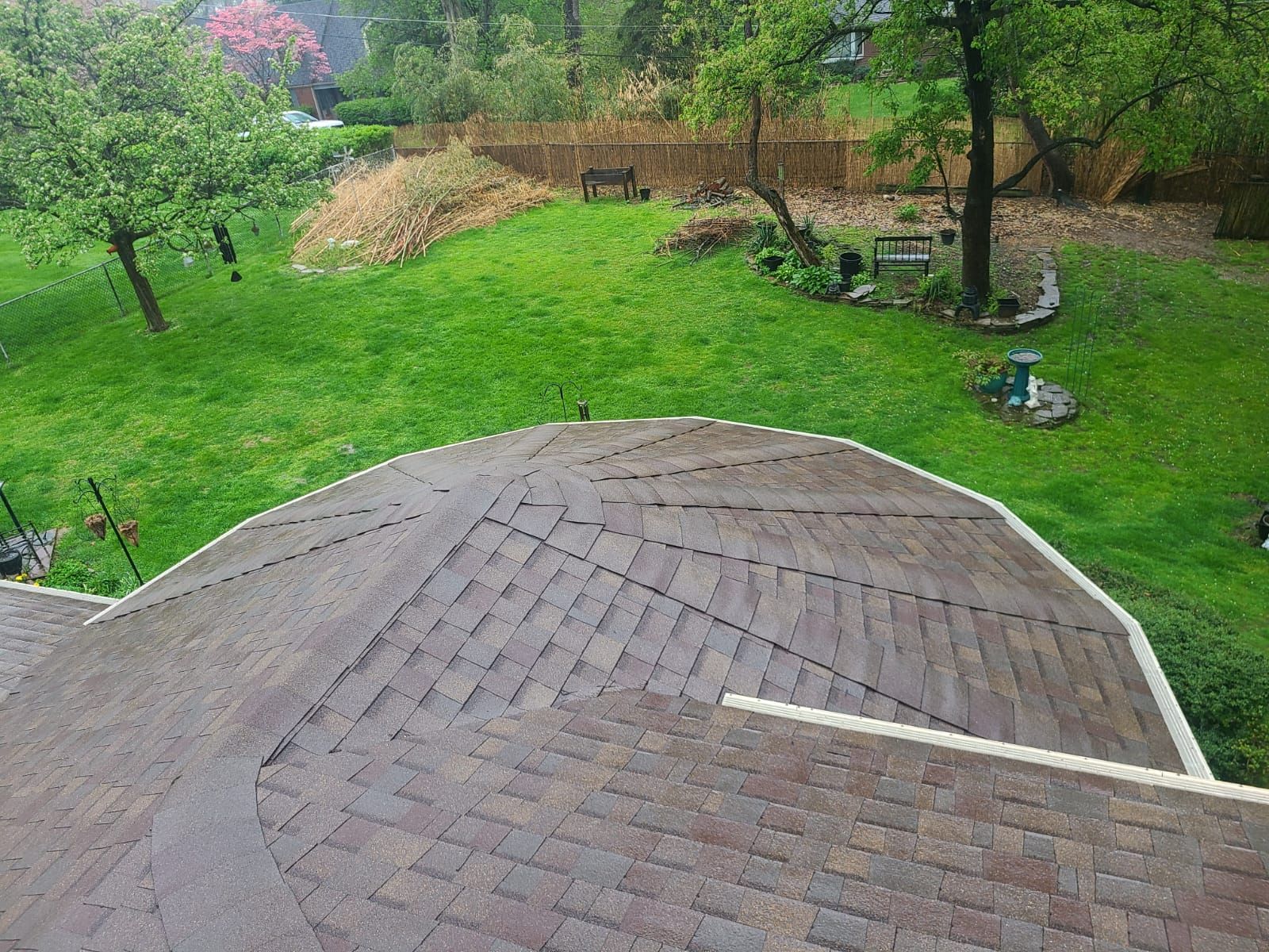 A brown shingled roof with a green lawn and trees in the background. Overcast day.