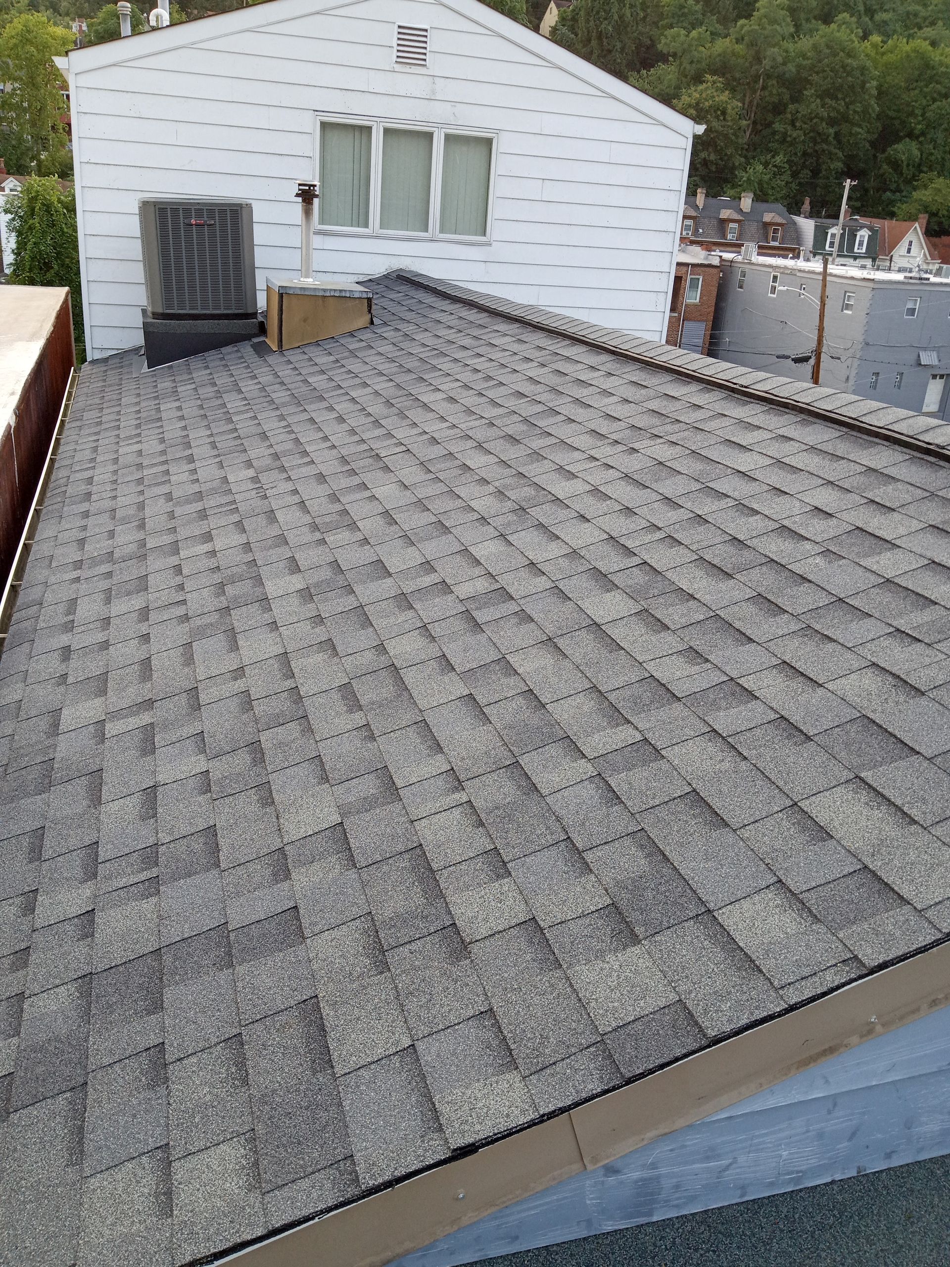 A gray shingle roof on a house, with an air conditioning unit visible.