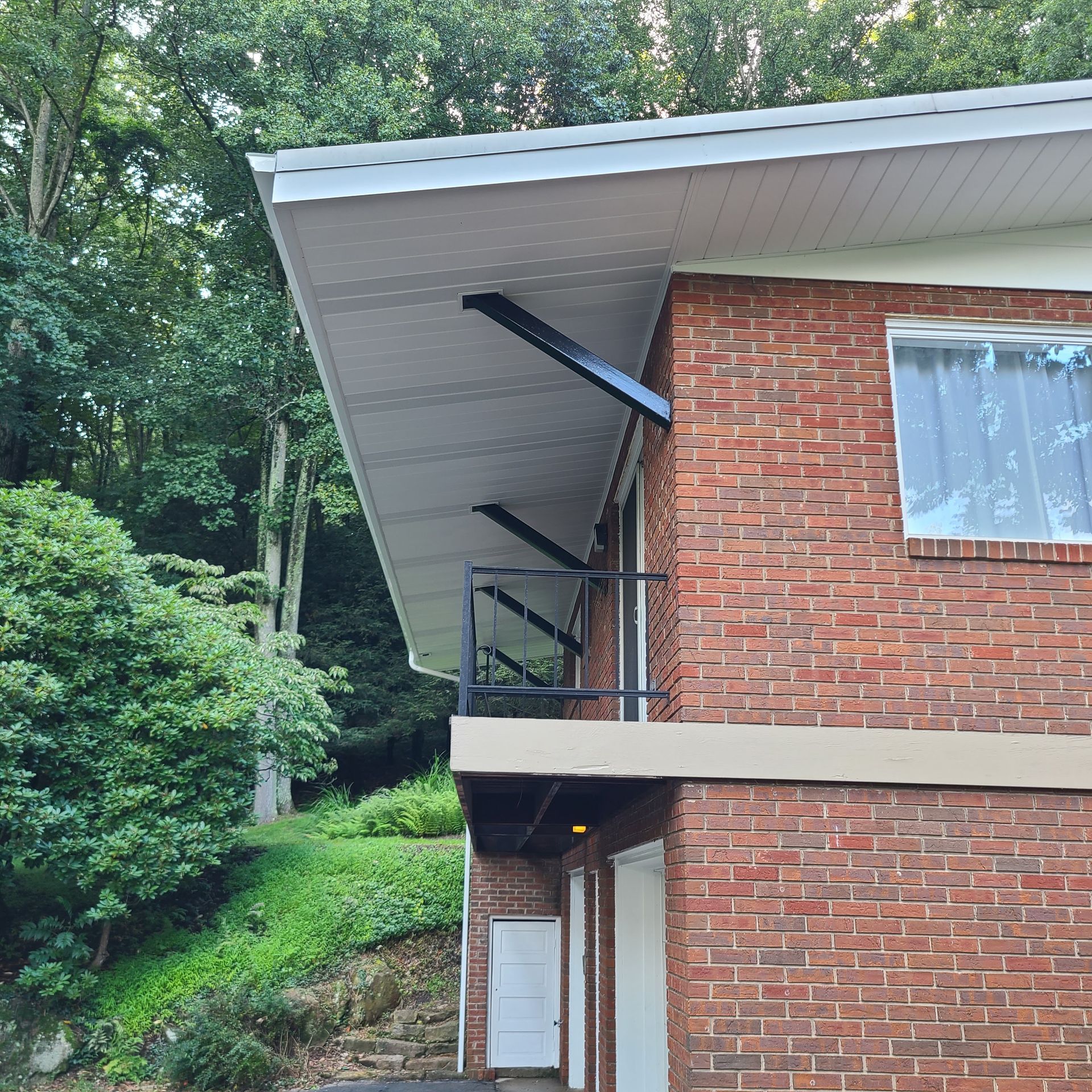 Brick house with white soffit, dark supports, and a small balcony. Trees in the background.
