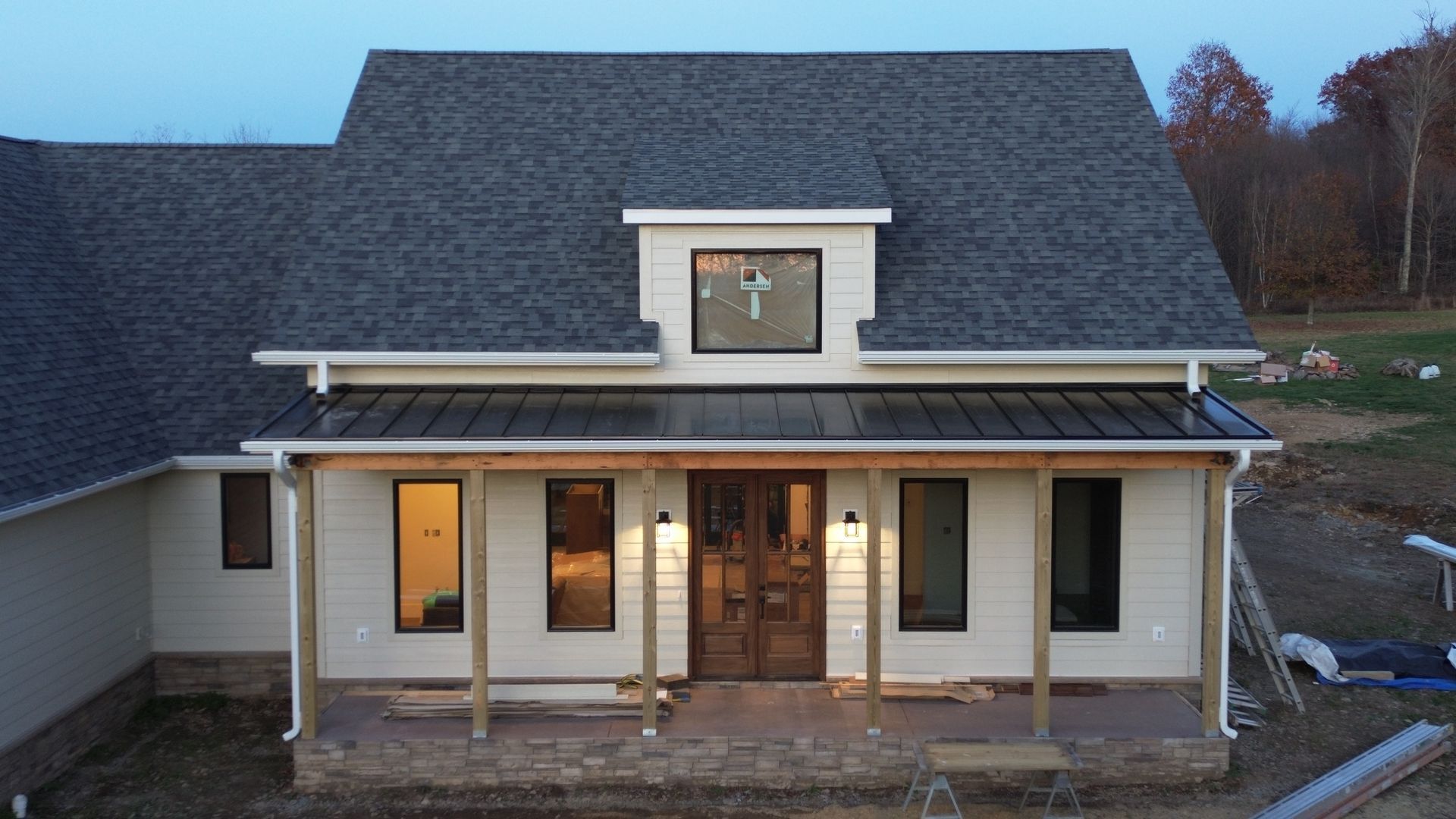 Exterior view of a newly-built house with a porch and dormer. Features gray roof, white siding, and brown wooden front door.