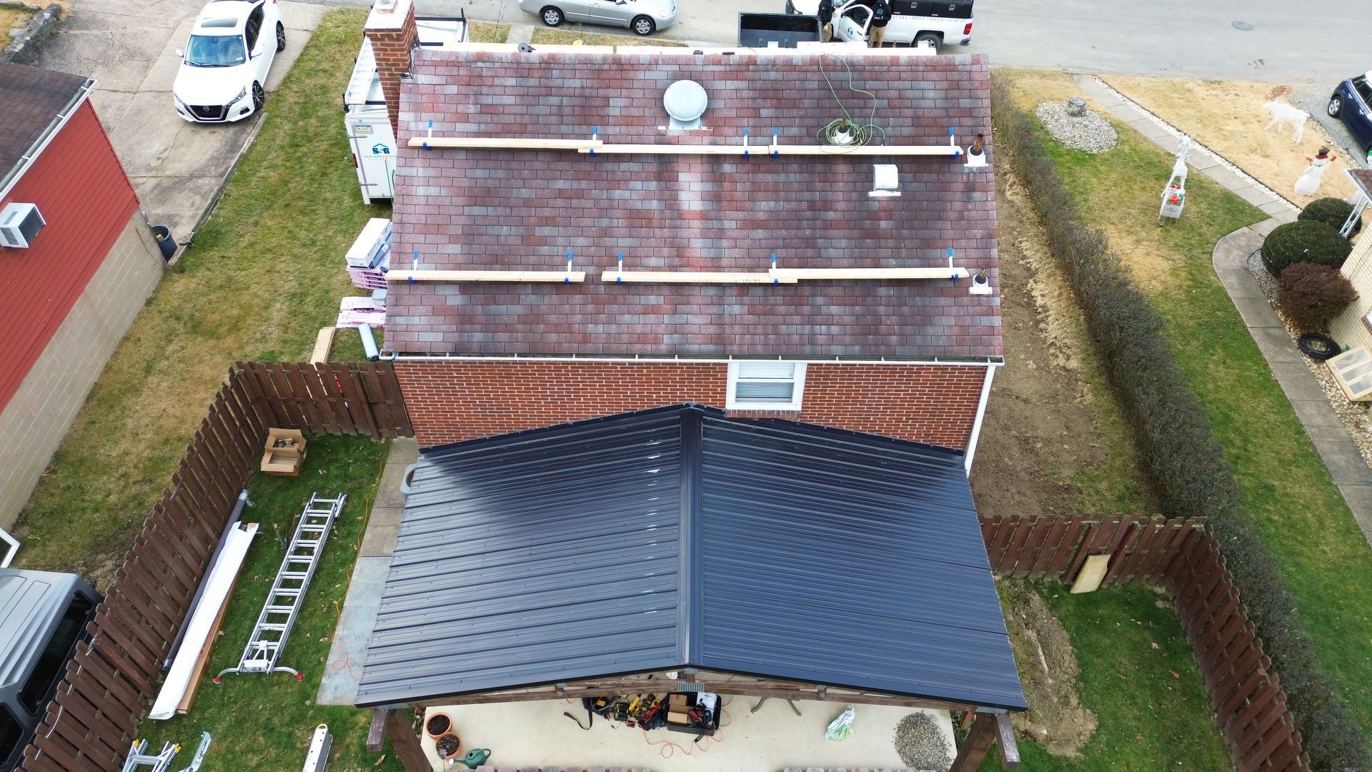 Overhead view of a house with a section of new black roof and old red roof. Wooden planks are laid across the older part.