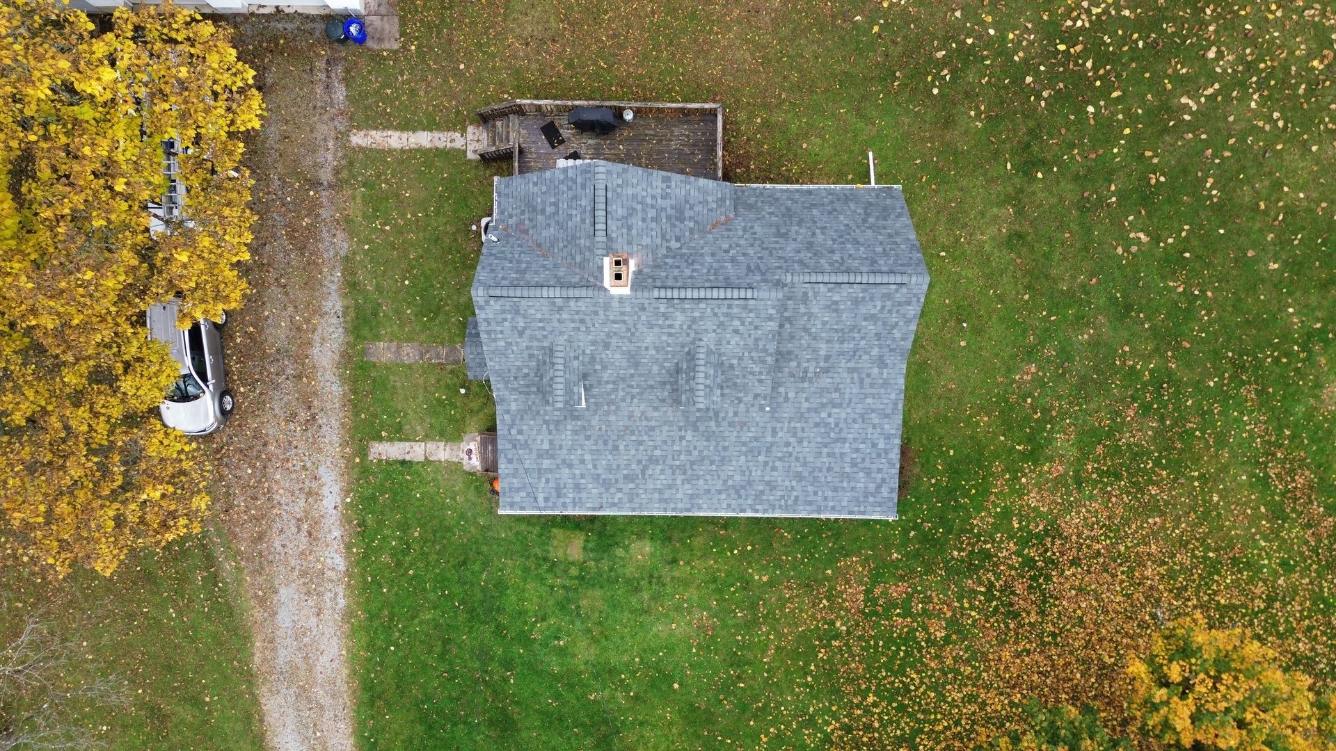 Overhead view of a house with a gray roof, chimney, and green and yellow foliage.