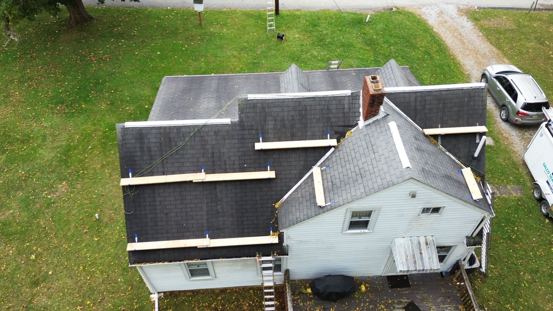Overhead view of a two-story house with a dark gray roof; wooden supports are visible. A car is parked in the driveway.