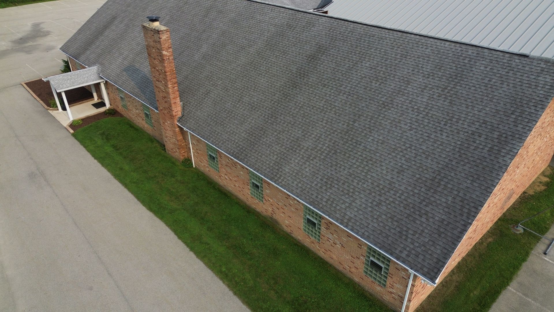 Overhead view of a house roof, covered in dark gray asphalt shingles with a chimney.