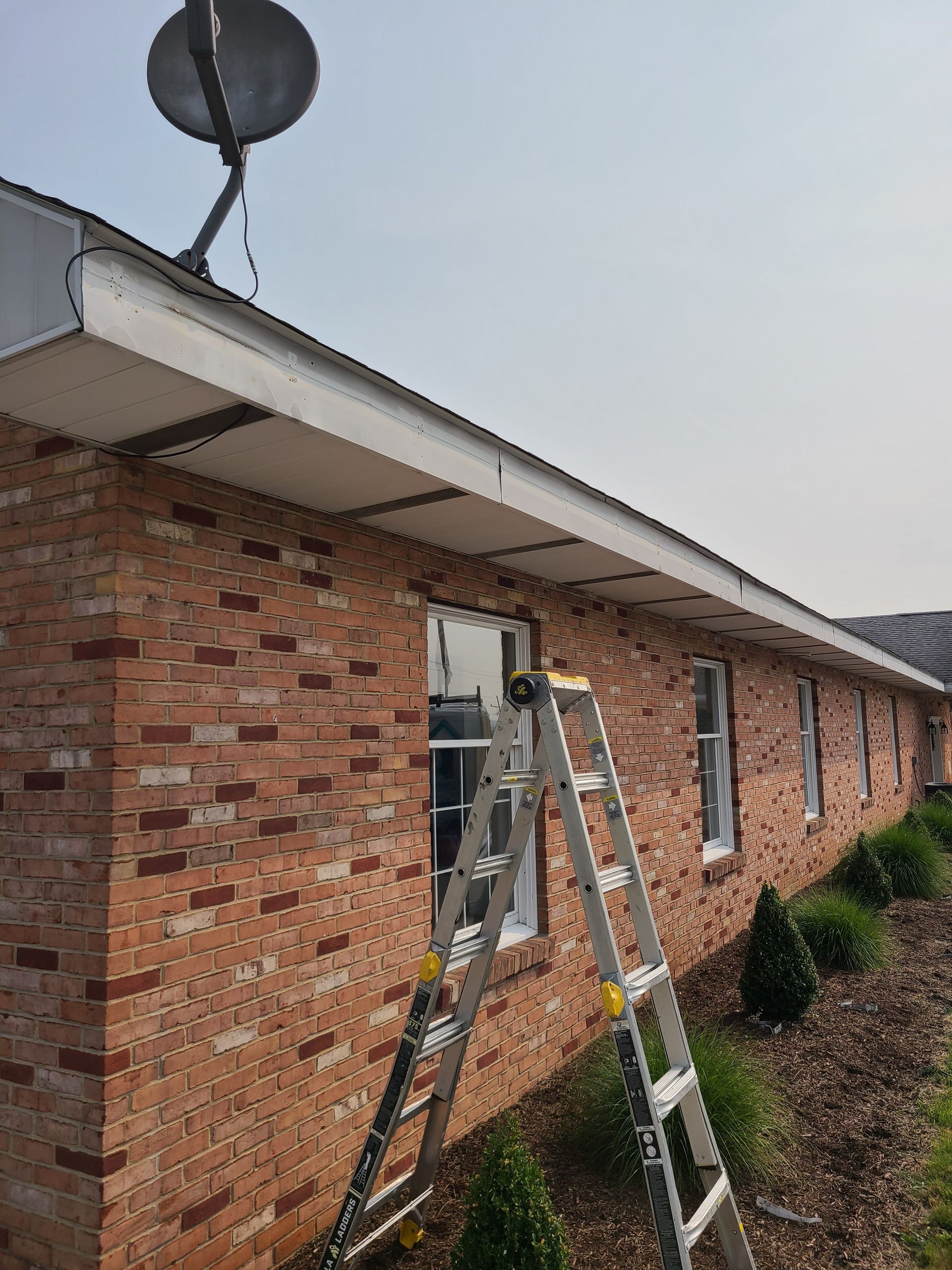 Beige roof overhang and gutter on brick building with dark roof tiles against a blue sky.