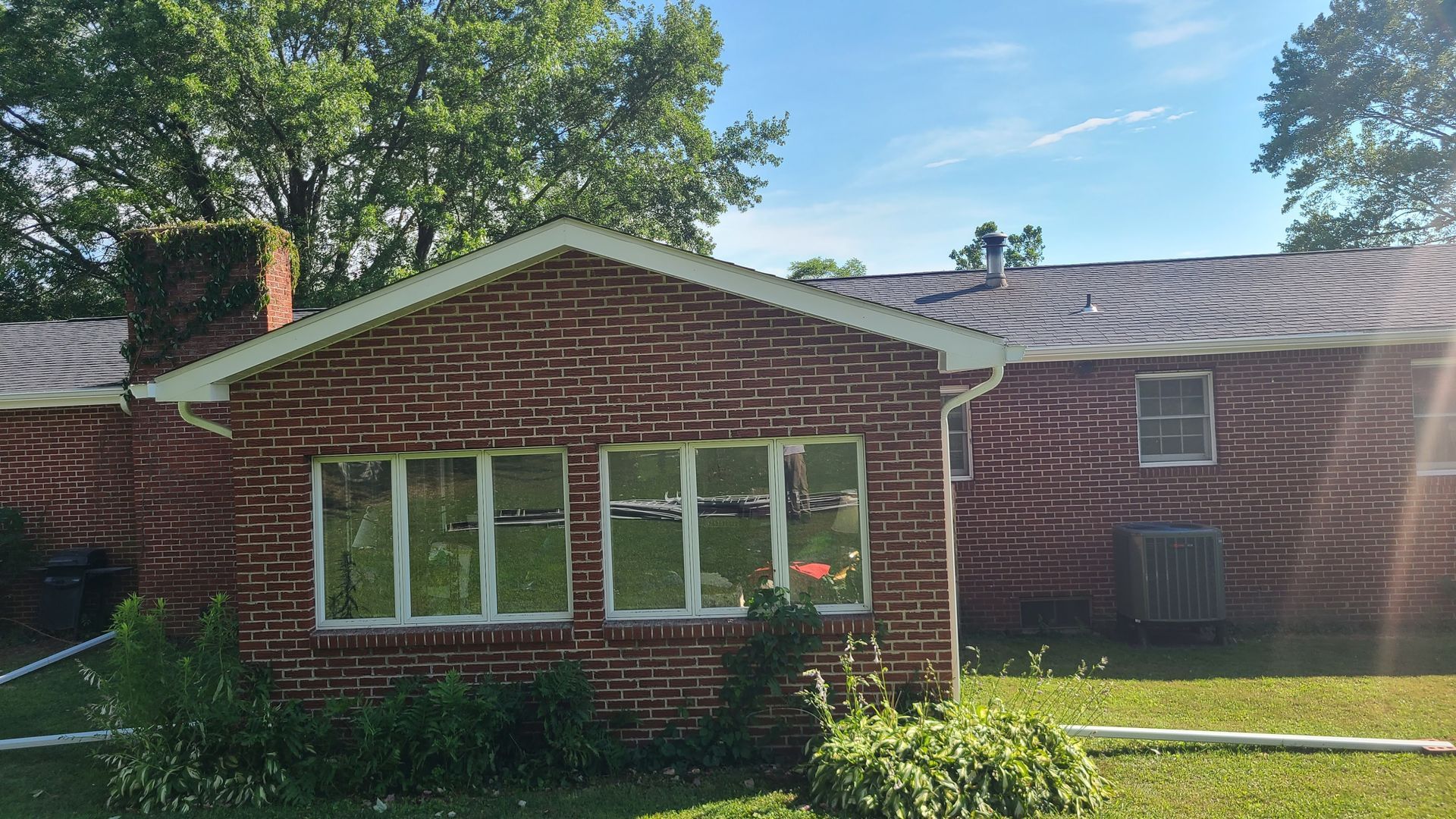 Beige siding on house with white gutters and trim against a background of fall foliage.