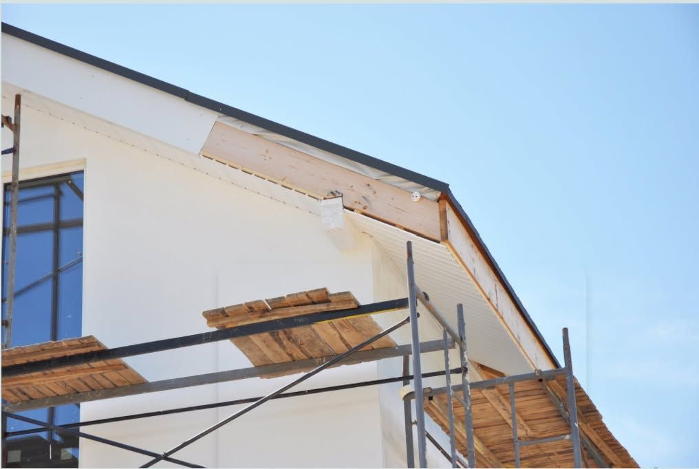 House exterior under construction, white walls, scaffolding, blue sky.