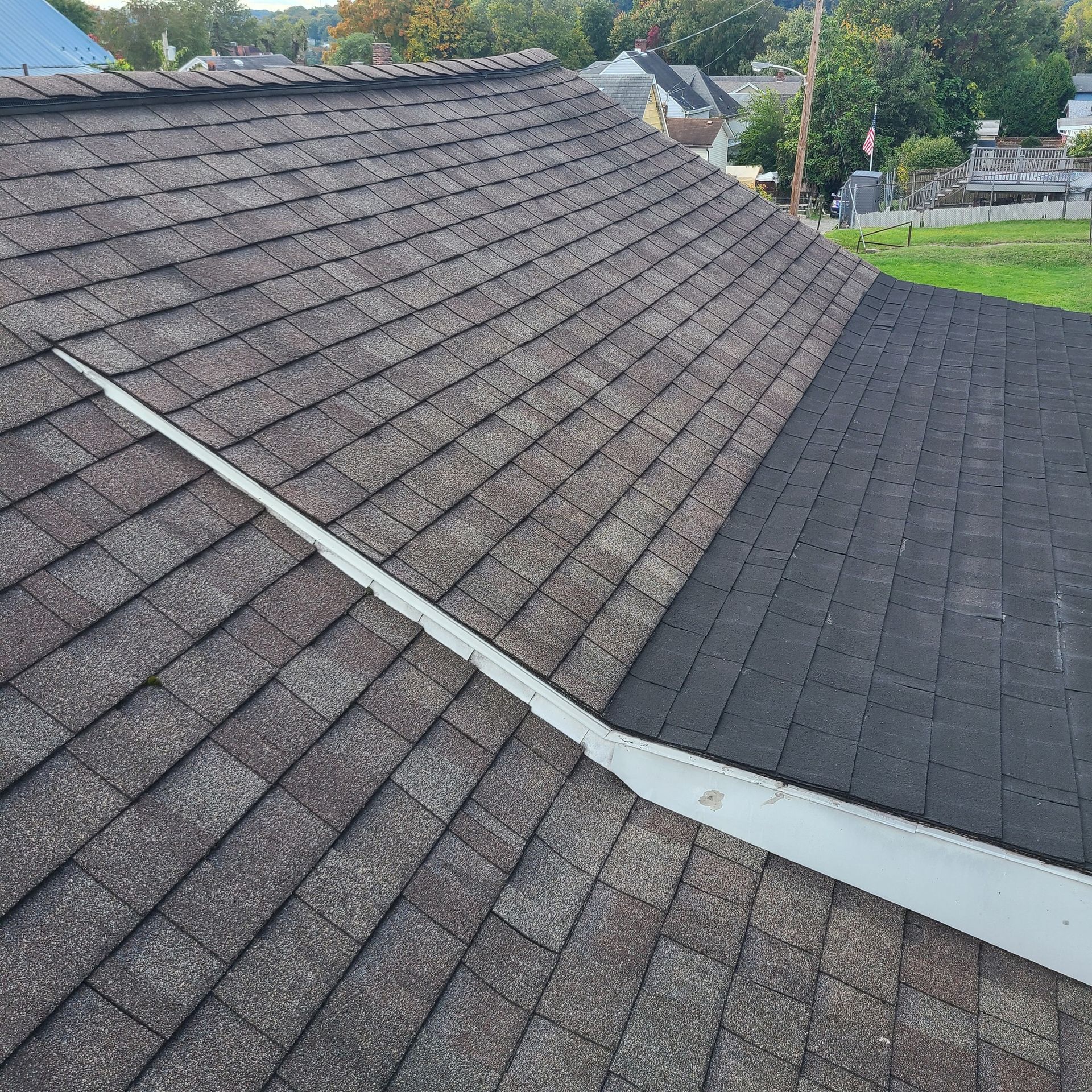 A partially shingled roof with a metal flashing. One section is dark, new shingles, the other is older, gray.