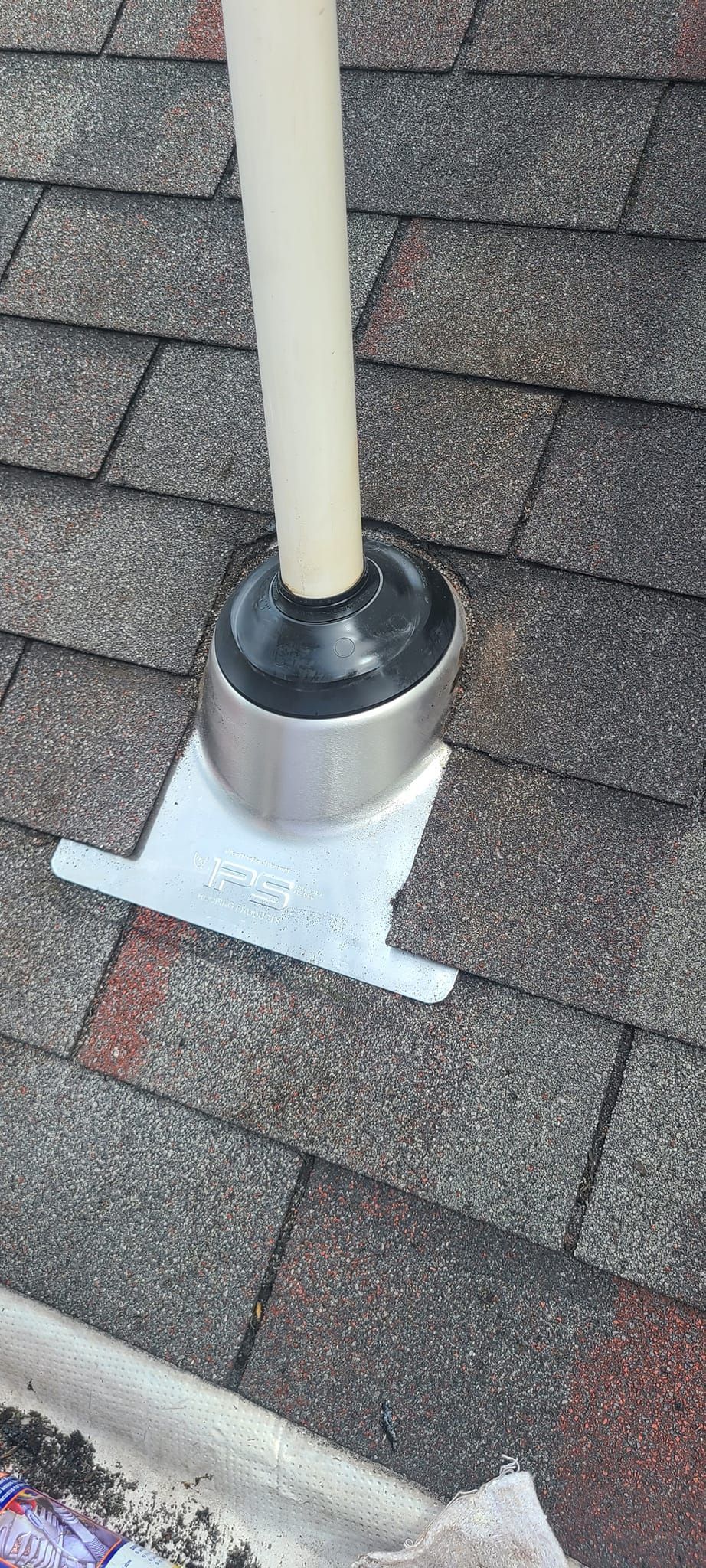Vent pipe flashing on a shingled roof, silver metal base with a black rubber boot.